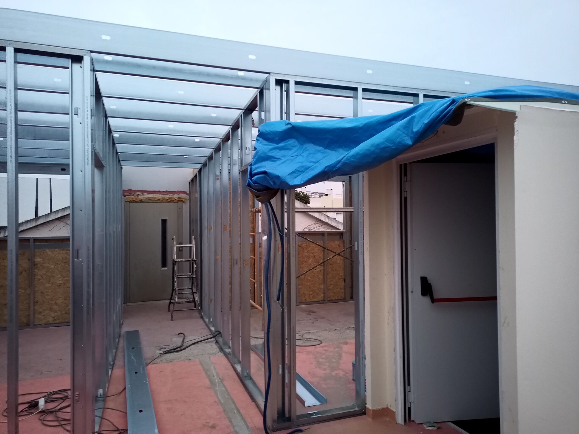 Construção de paredes e teto internos com estrutura metálica. Uma lona azul cobre a entrada.