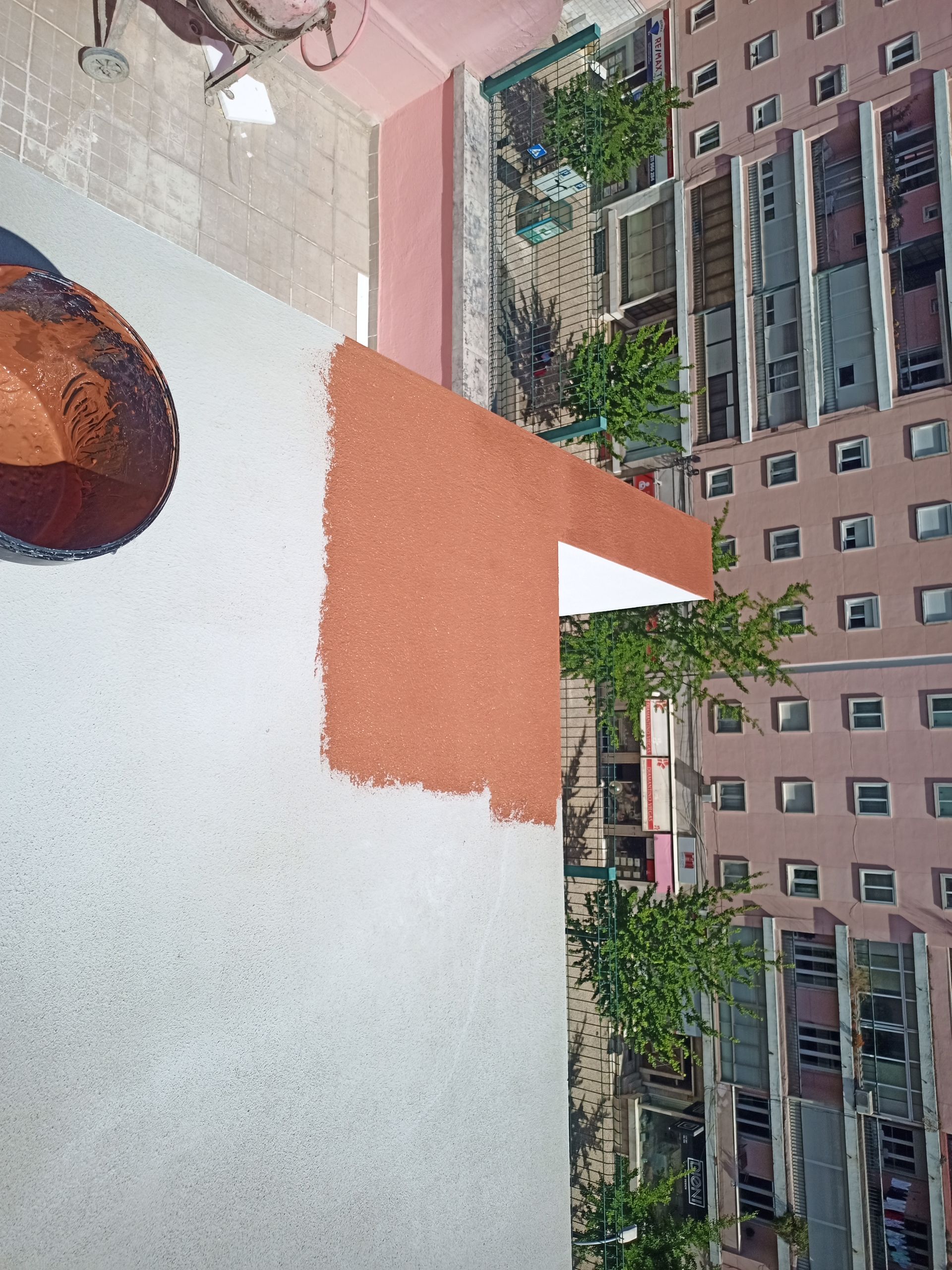 Vista aérea de edifícios com paredes em tons de vermelho-acastanhado e branco. Plantas e outras construções ao fundo.