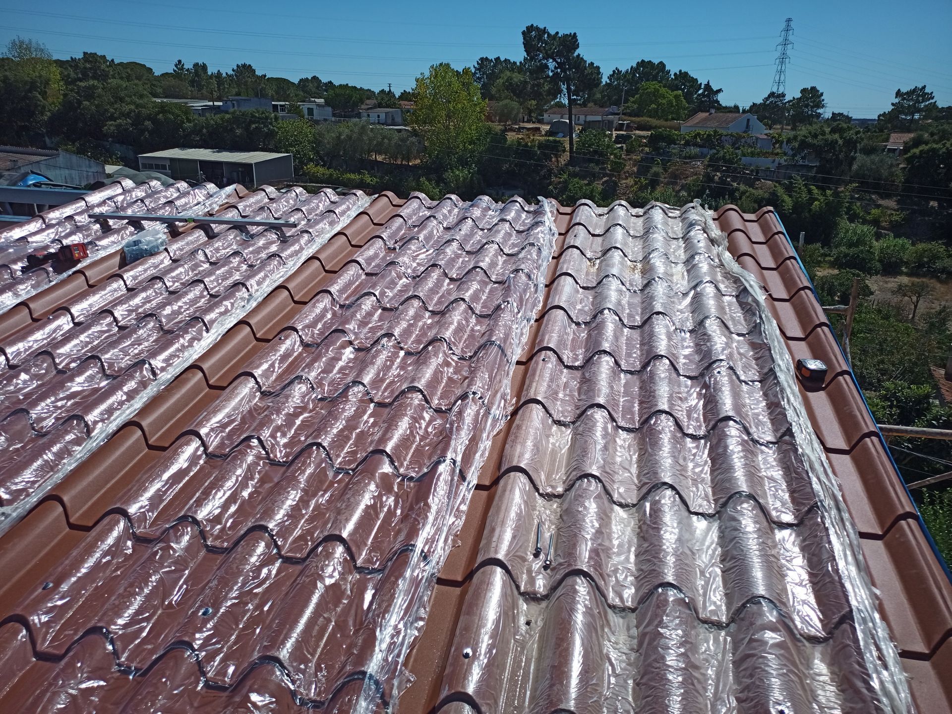 Telhado de metal ondulado marrom e transparente, com árvores e céu ao fundo.