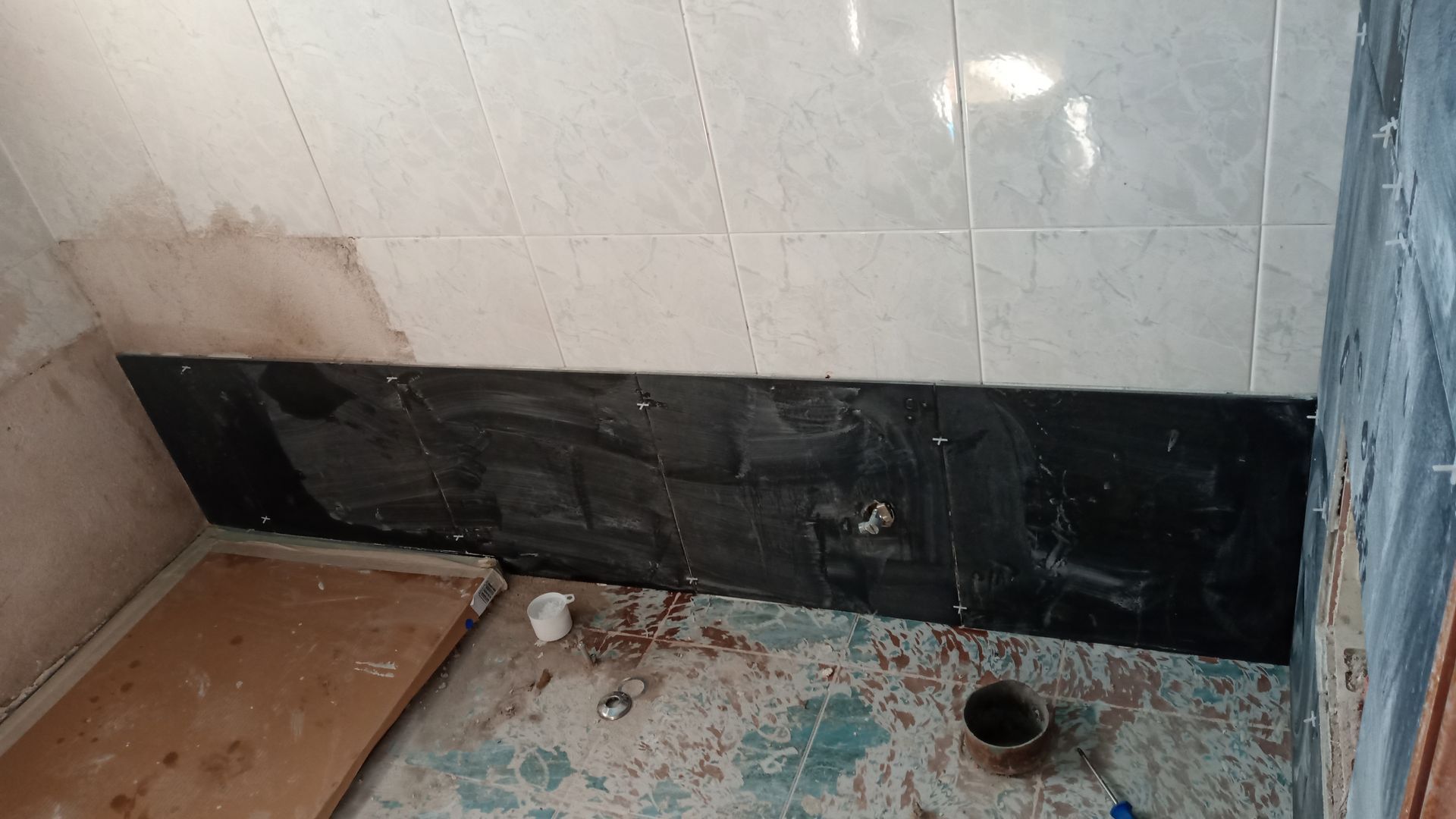 Banheiro em construção com base de azulejos pretos e azulejos bege acima.