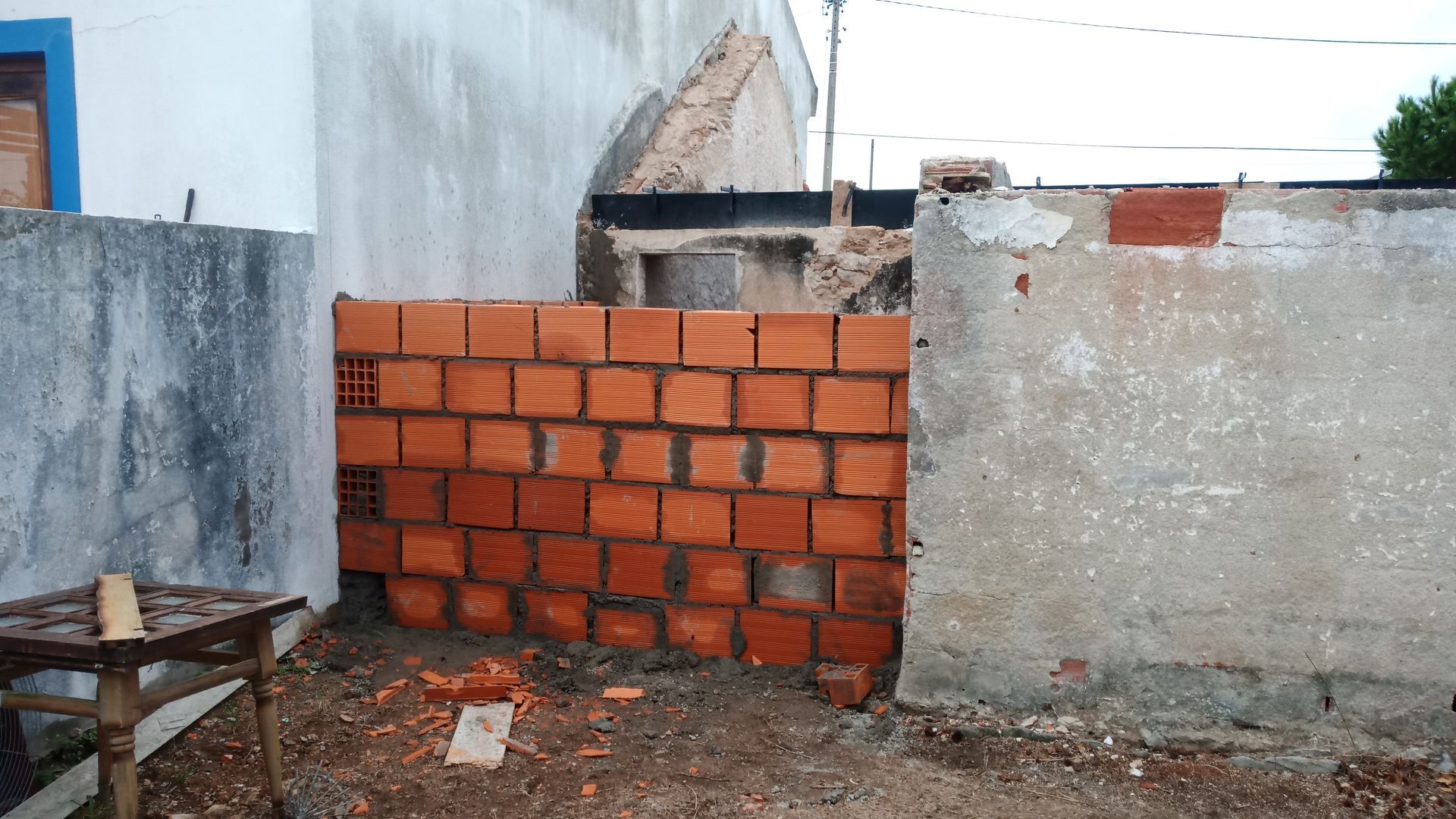 Parede de tijolos construída entre paredes de concreto; ambiente externo.