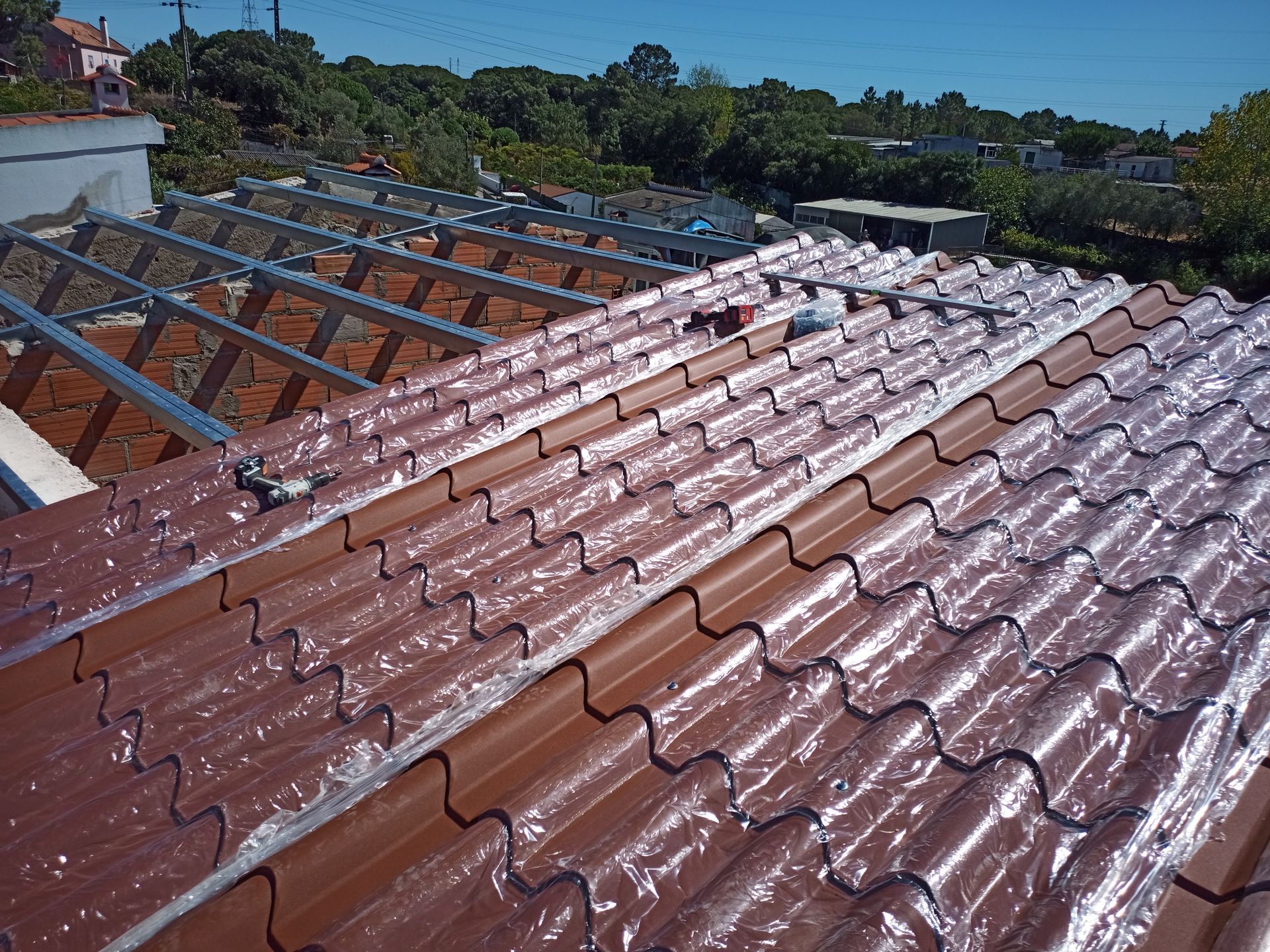 Telhado em construção com telhas marrons parcialmente cobertas com plástico.