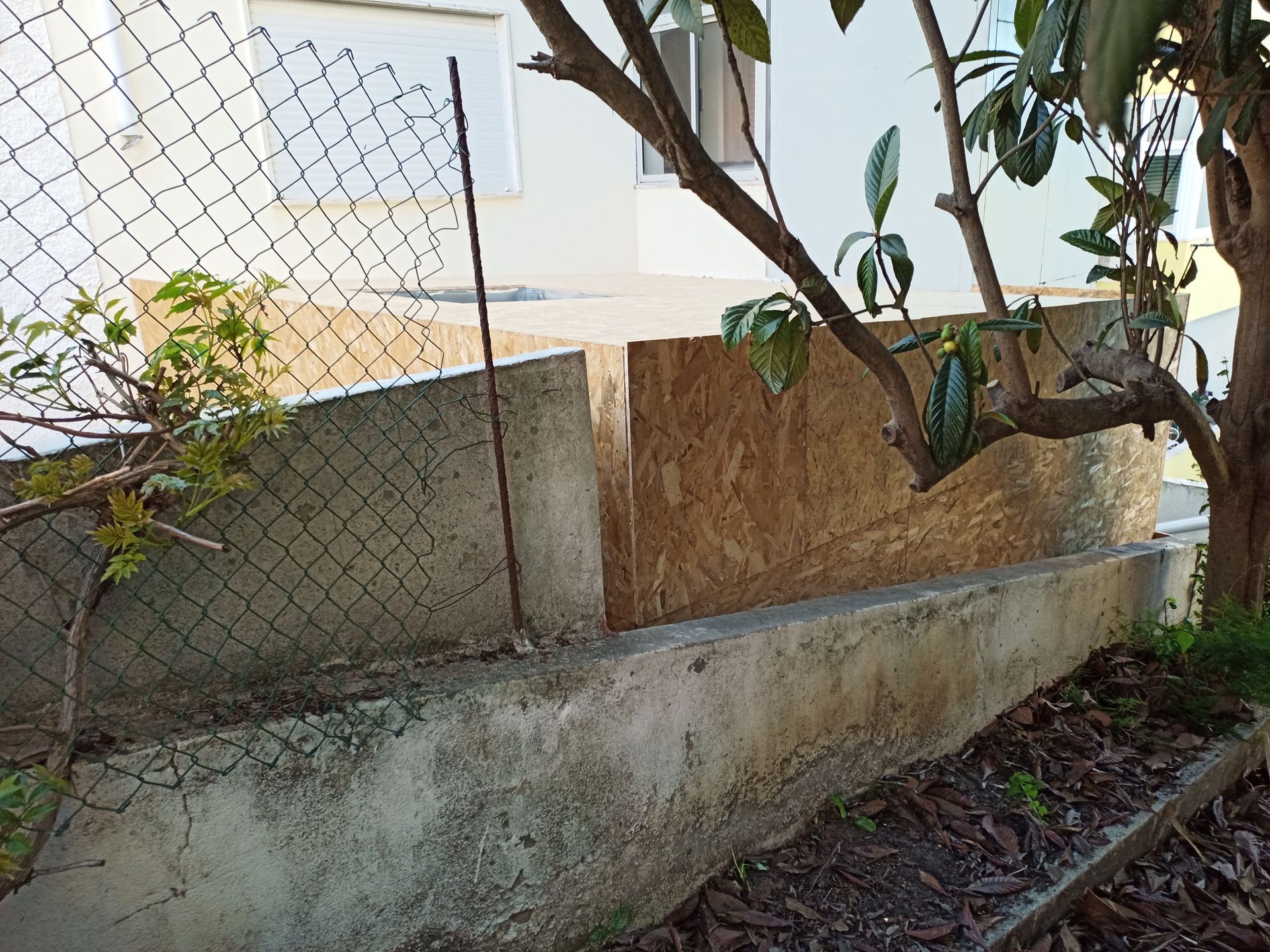 Muro de contenção de concreto com cerca de arame e painéis de madeira marrom. A vegetação está crescendo ao redor do muro.