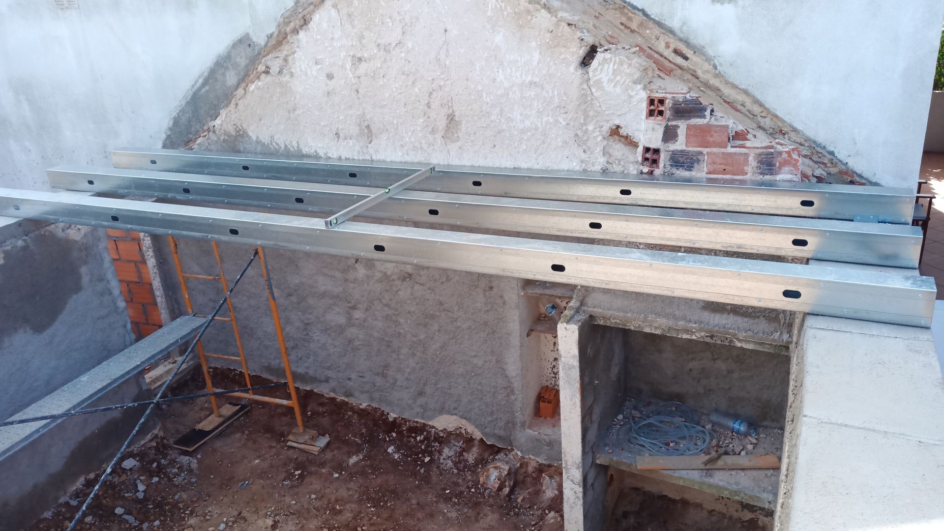 Canteiro de obras com vigas metálicas assentadas sobre uma estrutura de concreto e tijolos, possivelmente para um telhado ou plataforma.