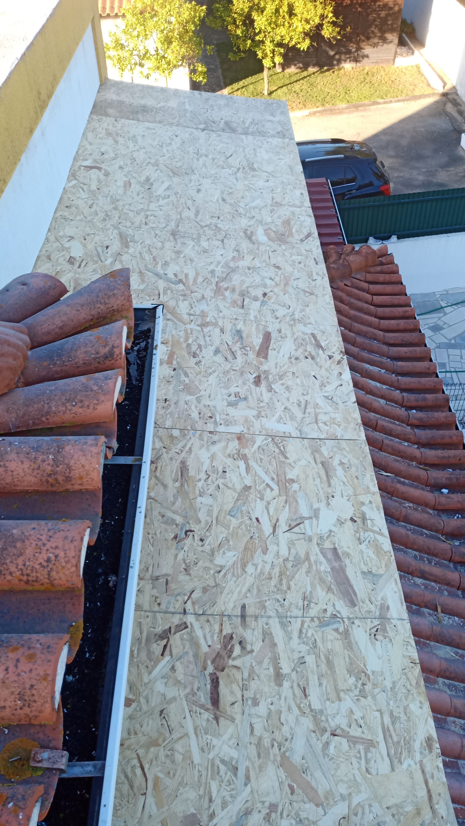 Trabalho de cobertura: Instalação de placas de OSB entre as telhas, com a calha e a estrutura do edifício visíveis.