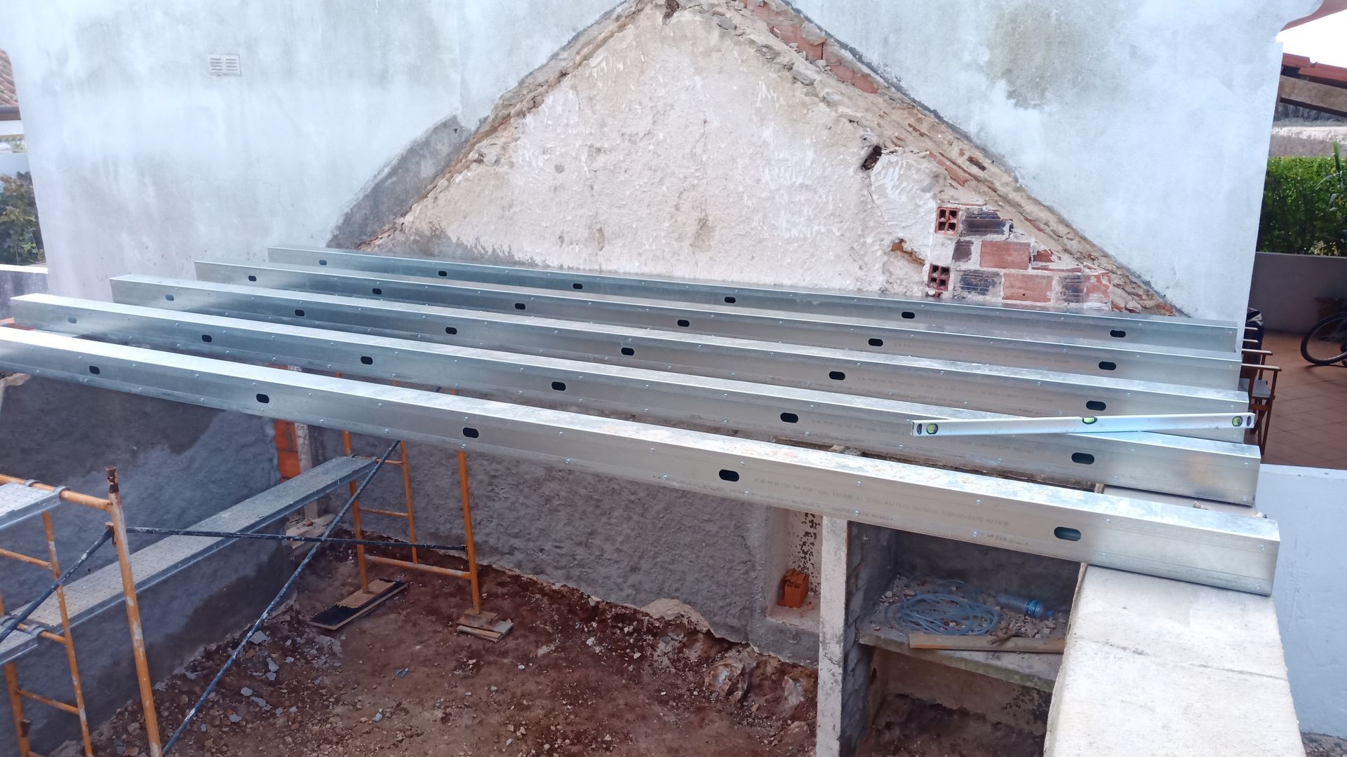 Canteiro de obras com vigas metálicas dispostas sobre uma estrutura, visto de baixo. Andaimes sustentam a estrutura parcialmente construída.