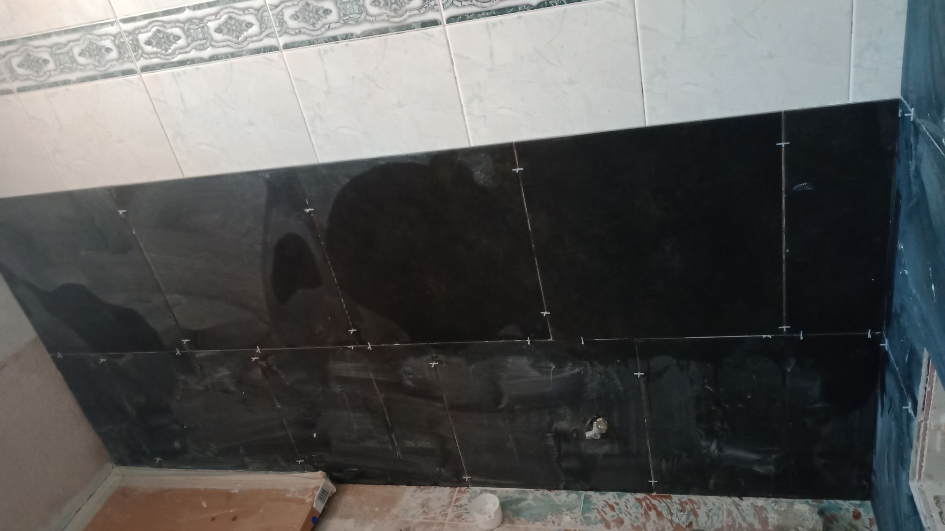 Azulejos pretos sendo instalados em uma parede, com espaçadores entre eles.