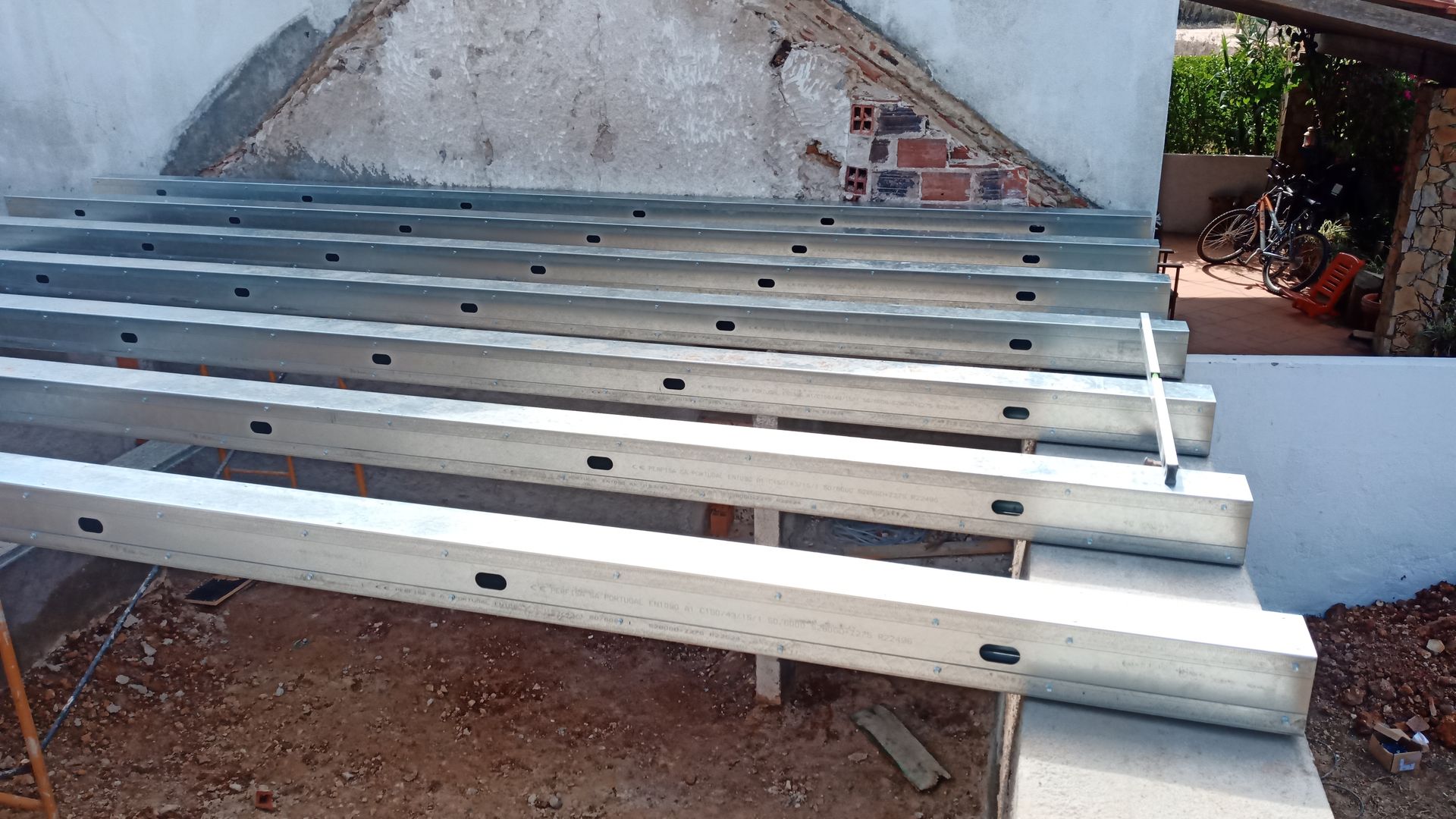 Vigas metálicas dispostas em fileiras, provavelmente para um deck ou pátio. Ambiente de construção.