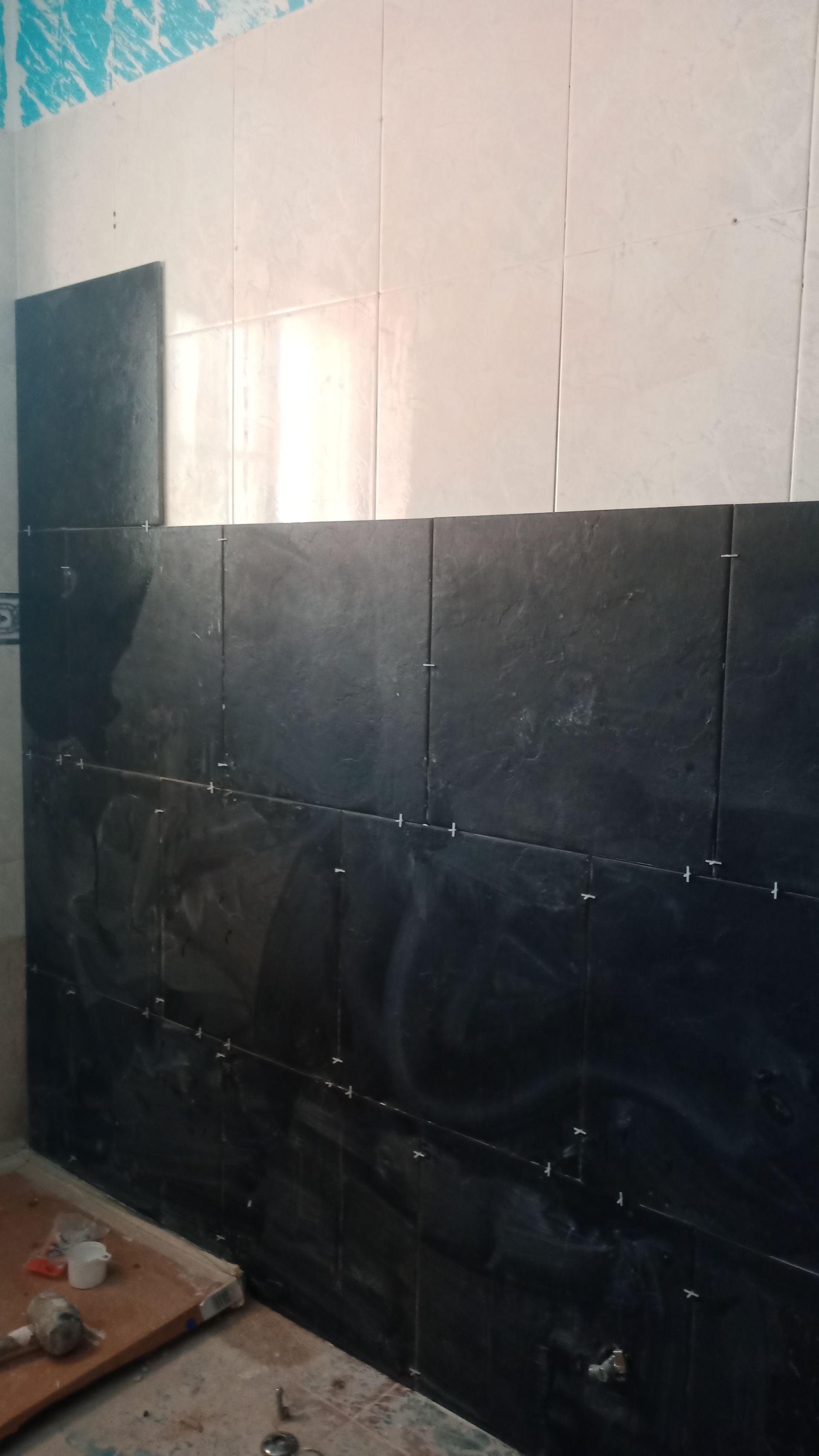 Azulejos pretos e brancos revestem parcialmente uma parede do banheiro; obra em andamento.