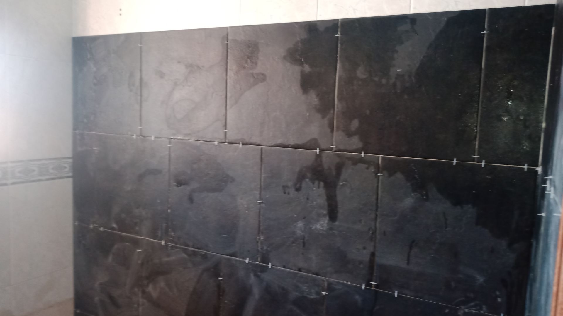 Parede de azulejos escuros em construção, espaçadores já instalados.