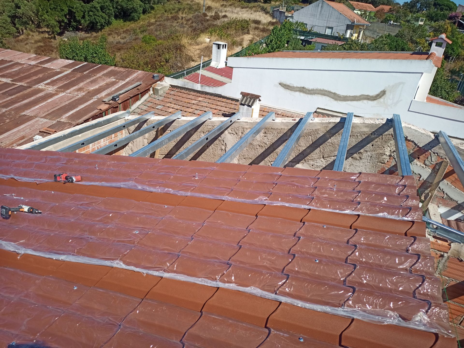 Vista do telhado de telhas de terracota em construção, mostrando as estruturas metálicas de suporte e parte do telhado recém-coberto com telhas.