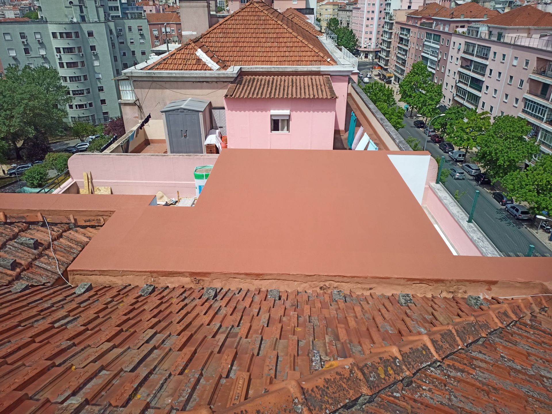 Vista de um telhado de telhas de terracota, mostrando um telhado plano, marrom-avermelhado, e edifícios da cidade.