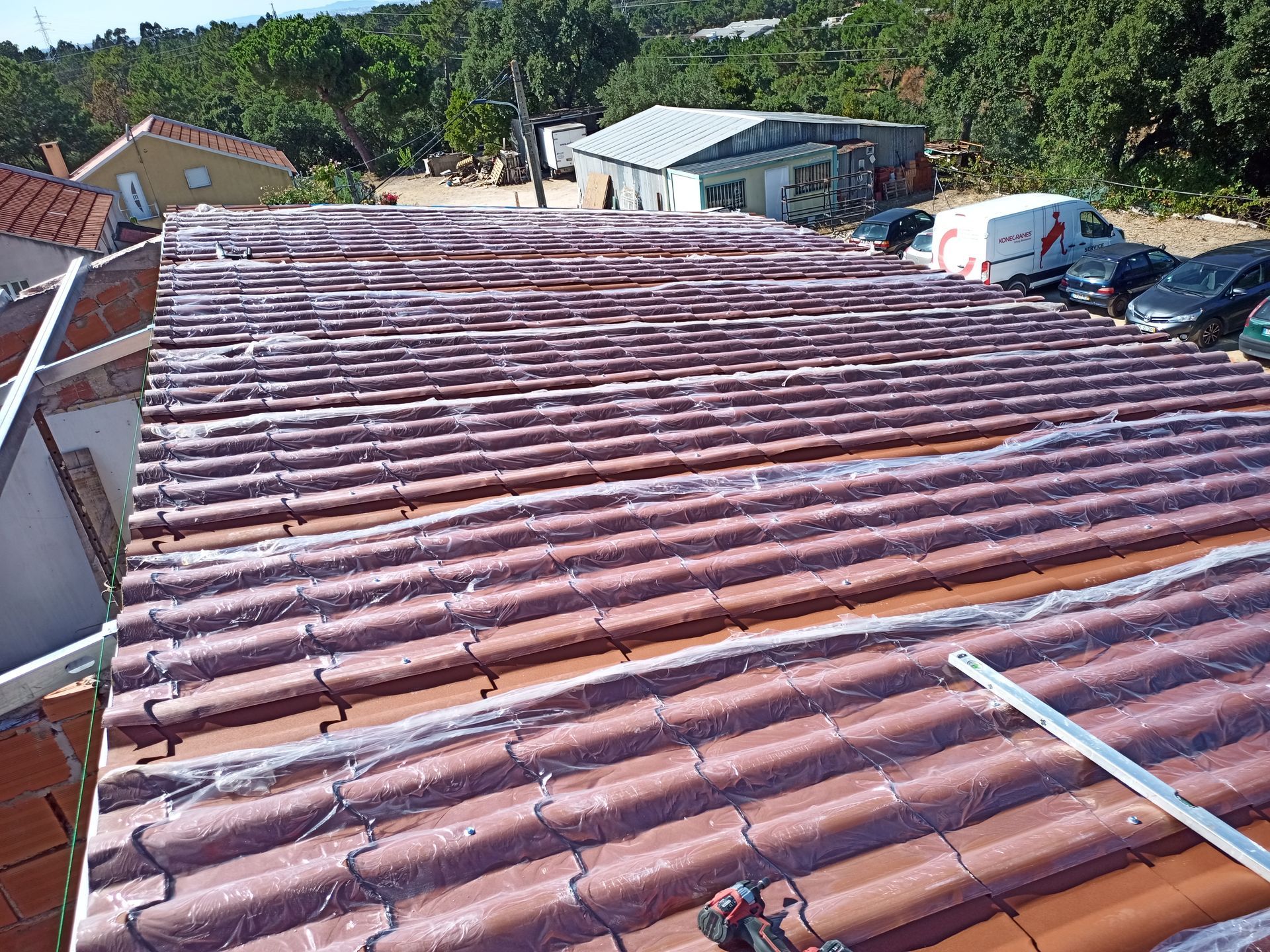 Telhado de telhas vermelhas com cobertura transparente. Árvores e edifícios ao fundo. Ambiente externo ensolarado.
