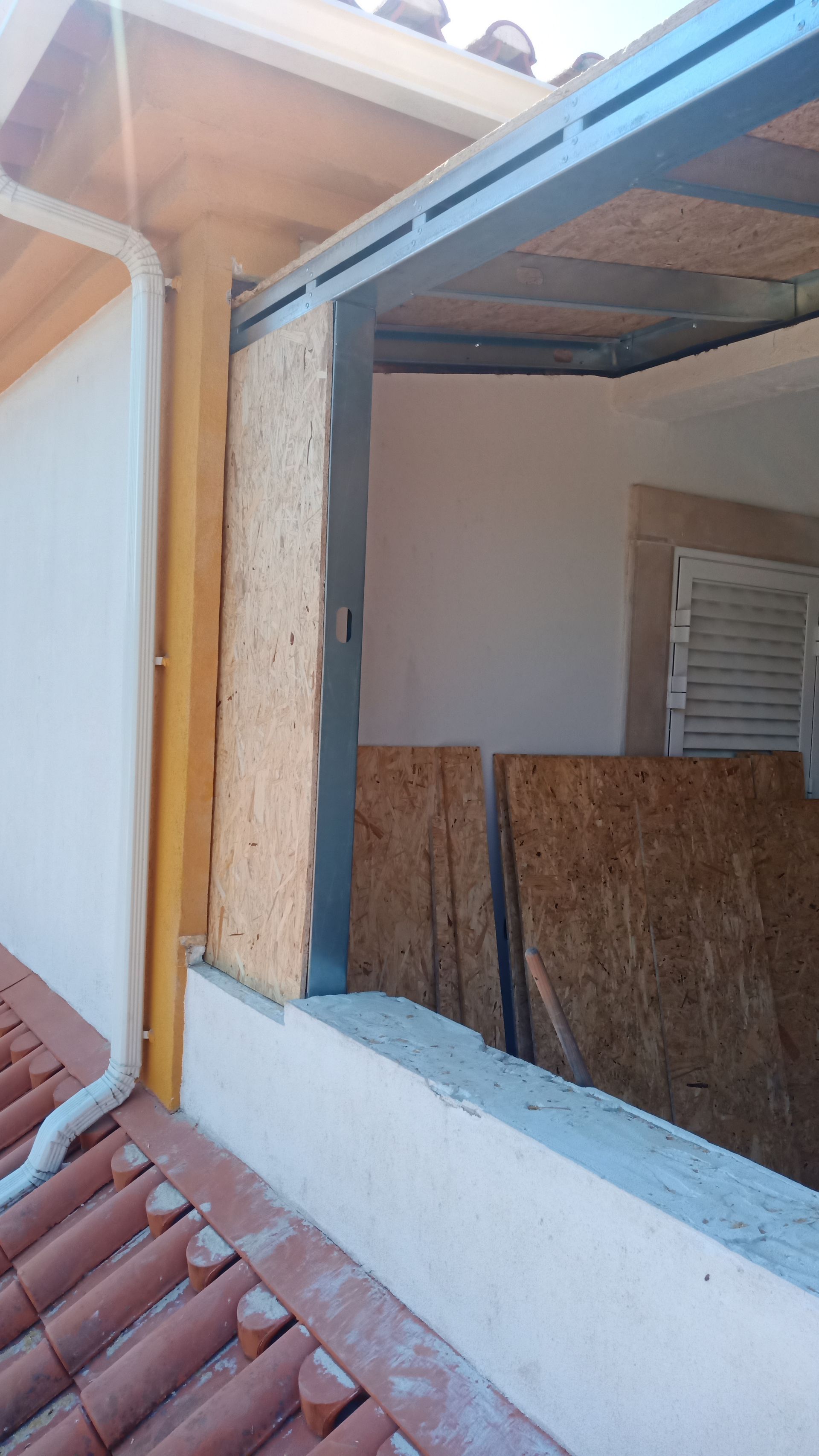 Canteiro de obras, vista externa. Parede parcialmente construída com painéis de madeira e estrutura metálica.