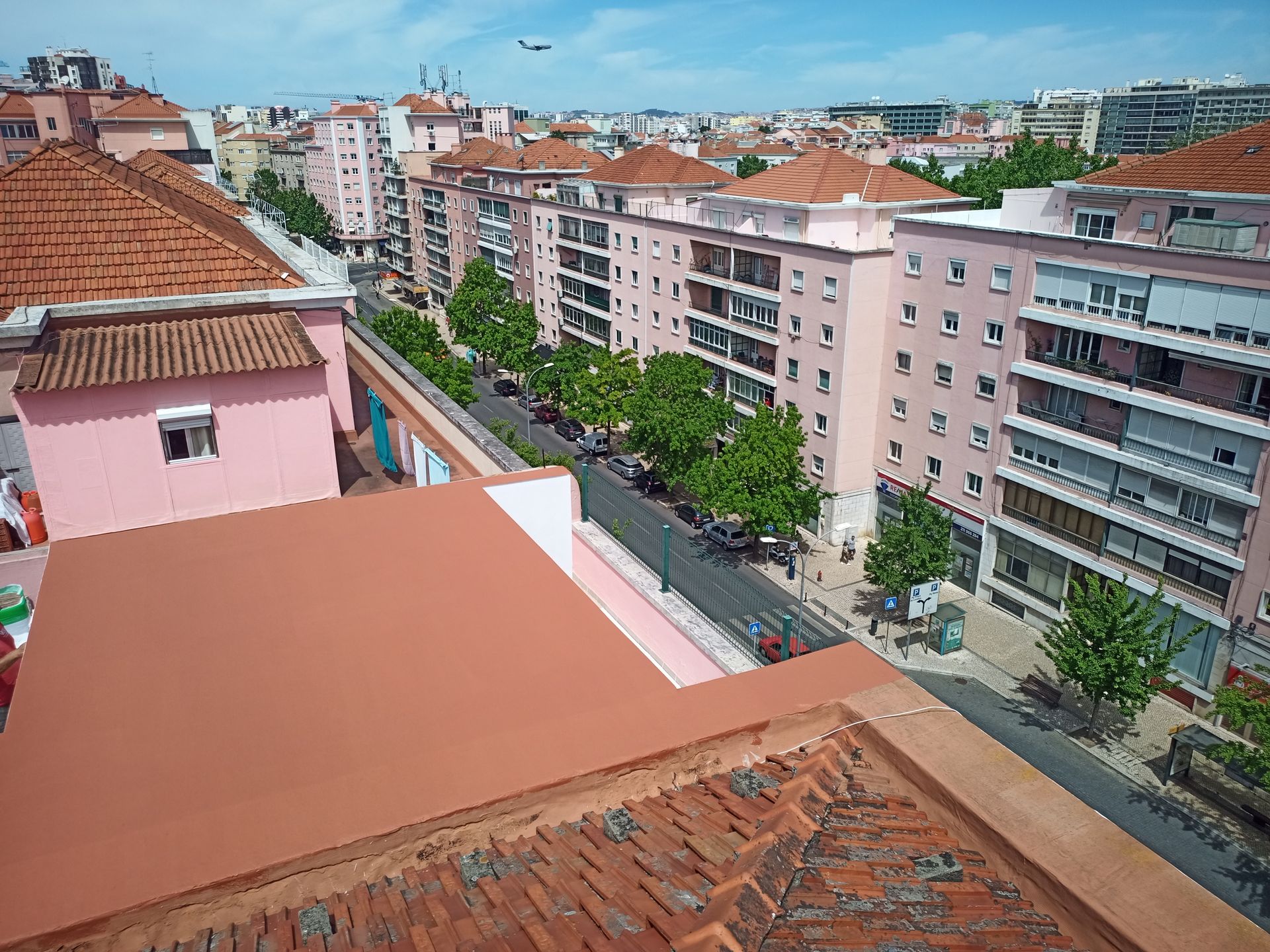 Vista de edifícios em Lisboa com telhados de terracota, fachadas cor-de-rosa e uma rua arborizada.