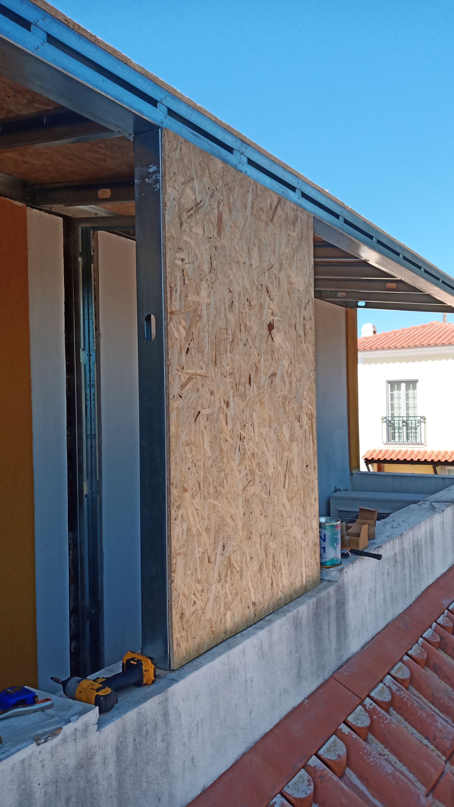 Construção de uma parede com um painel de madeira fixado a uma estrutura metálica, em um telhado.