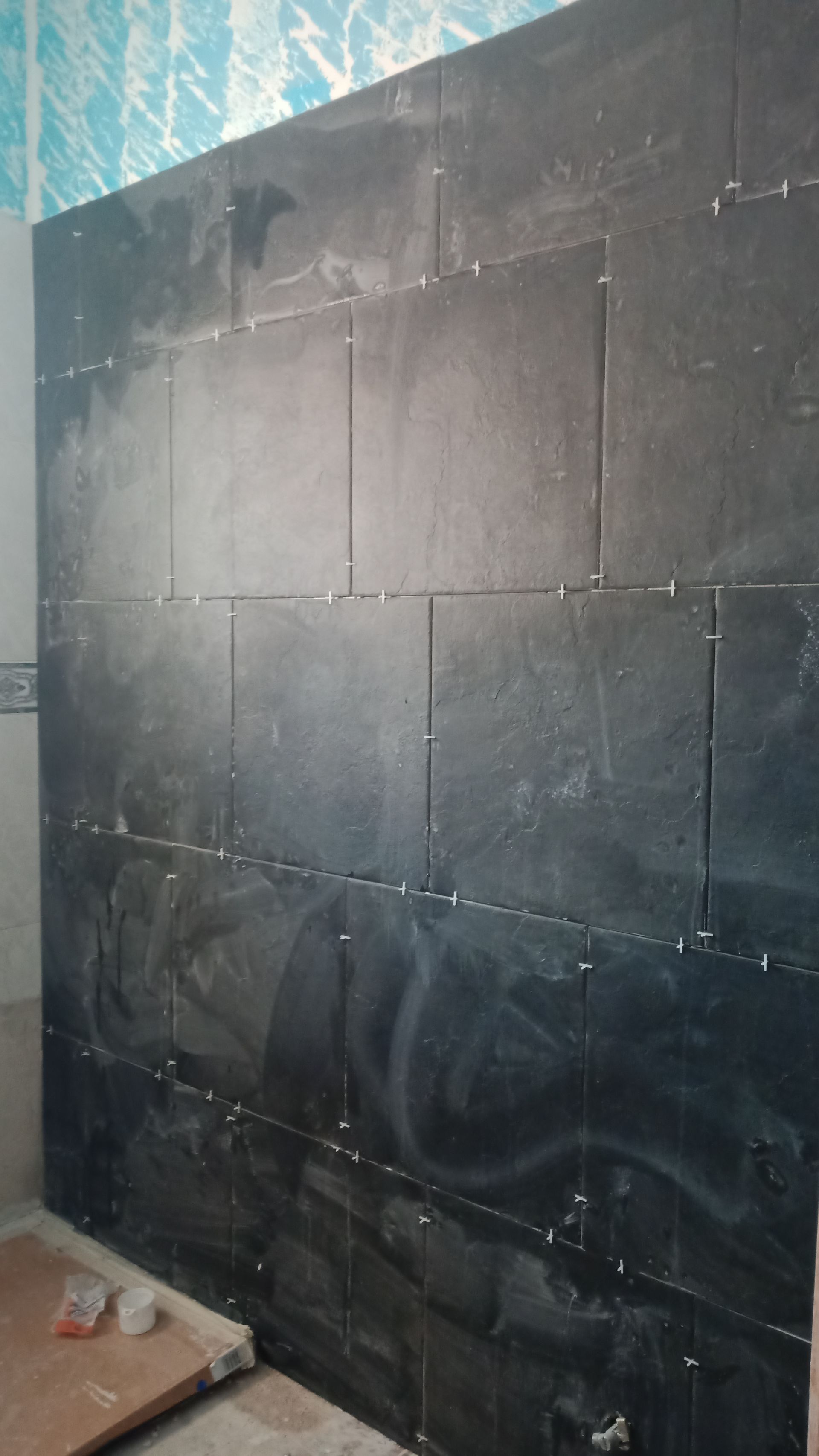 Parede do banheiro revestida com azulejos pretos em construção, com parede acima em tons de azul claro e branco.