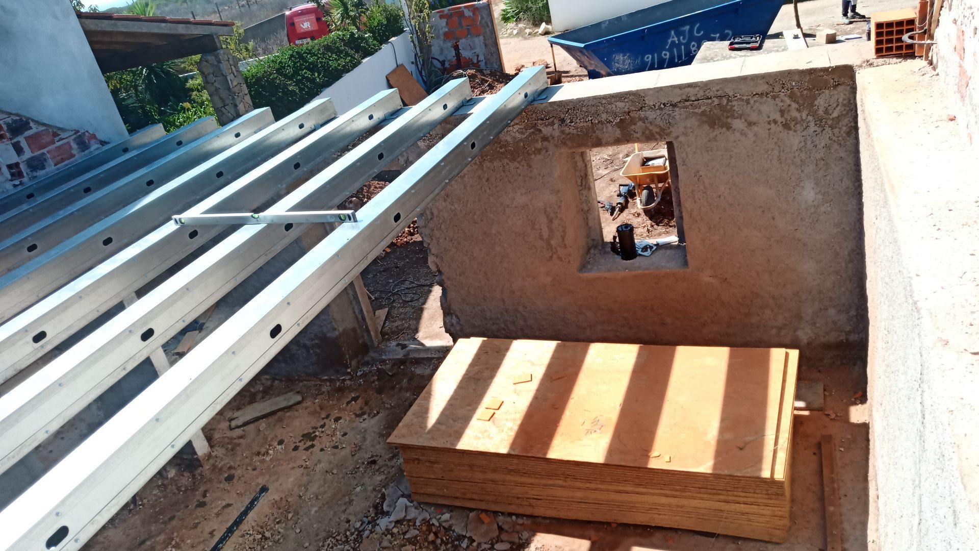 Canteiro de obras com uma escada metálica encostada na parede, isolamento e uma janela aberta.