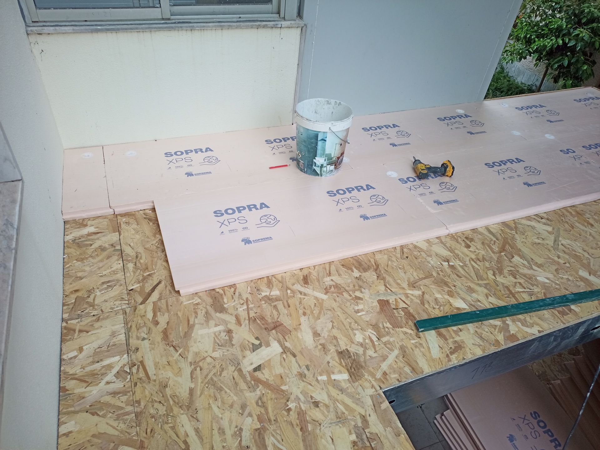 Subpiso de OSB com painéis de isolamento rosa sendo instalado; balde e ferramentas em cima.