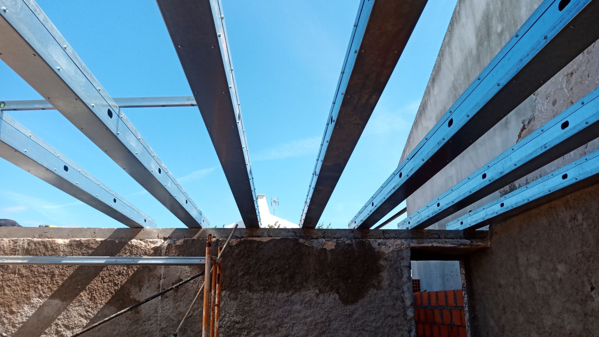 Vigas de aço formando a estrutura do telhado contra um céu azul claro.