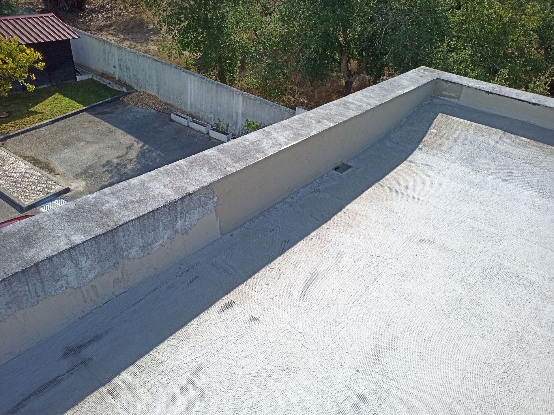 Cobertura de concreto com muro baixo, com vista para um quintal e árvores em um dia ensolarado.