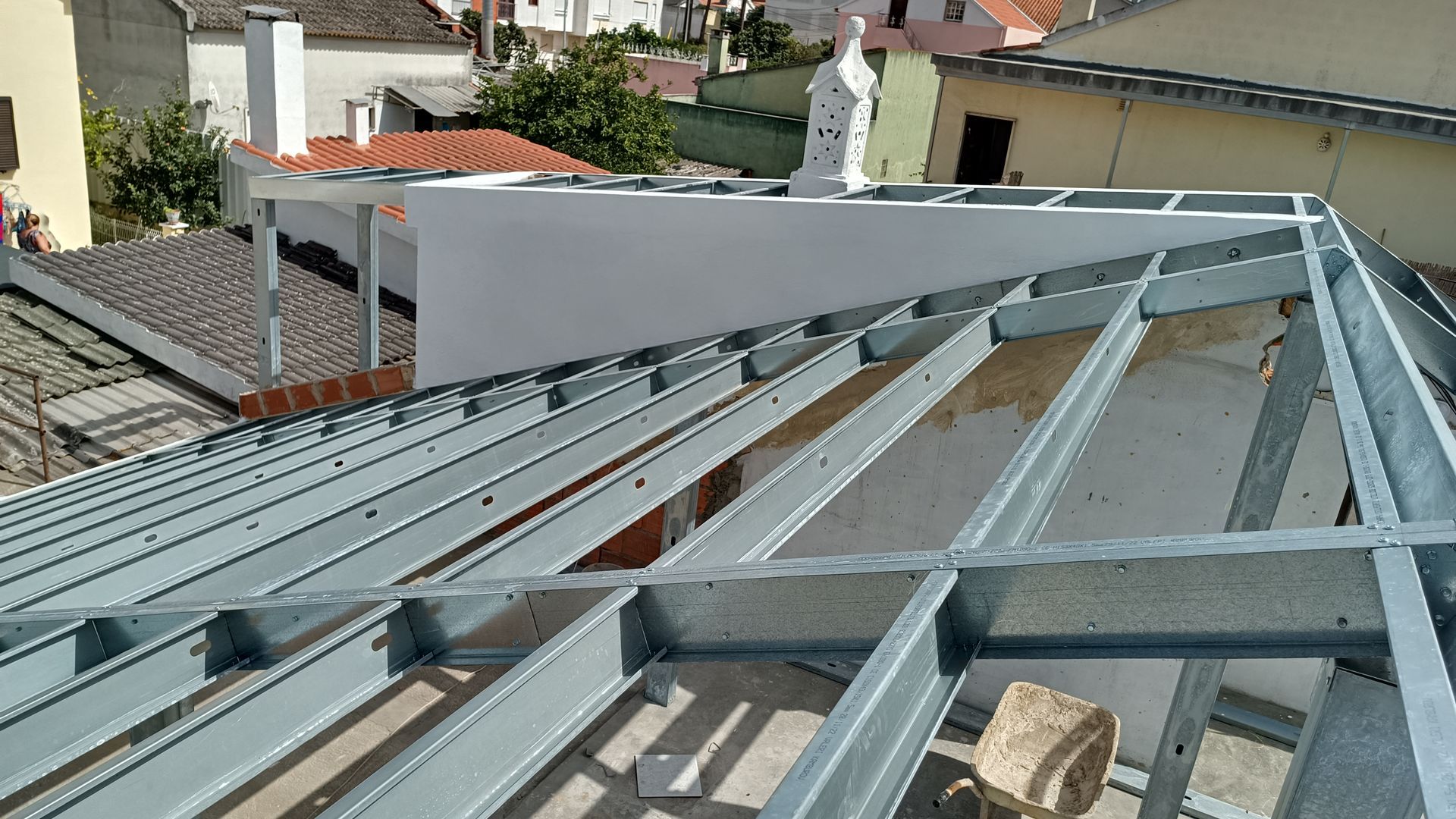 Estrutura metálica do telhado em construção, com paisagem urbana ao fundo.