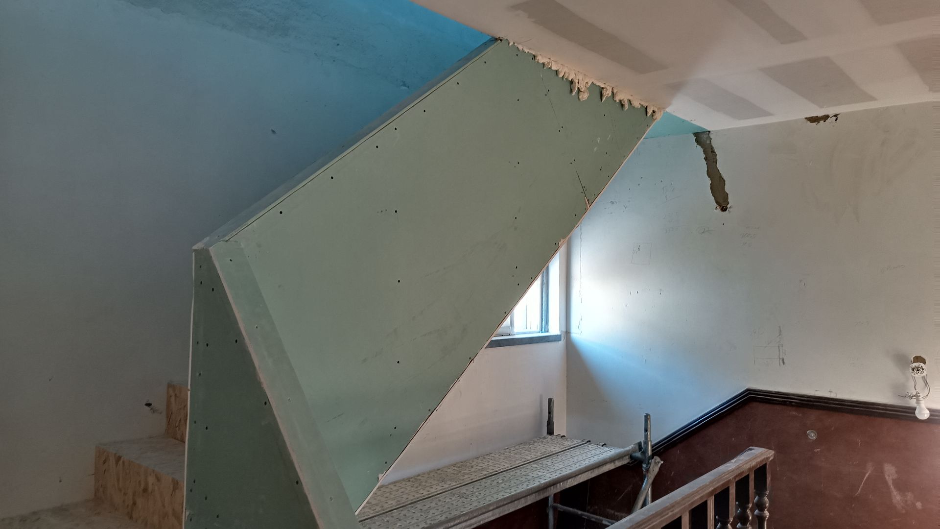 Escada em construção: instalação de drywall nas paredes e no vão da escada, com uma janela visível.