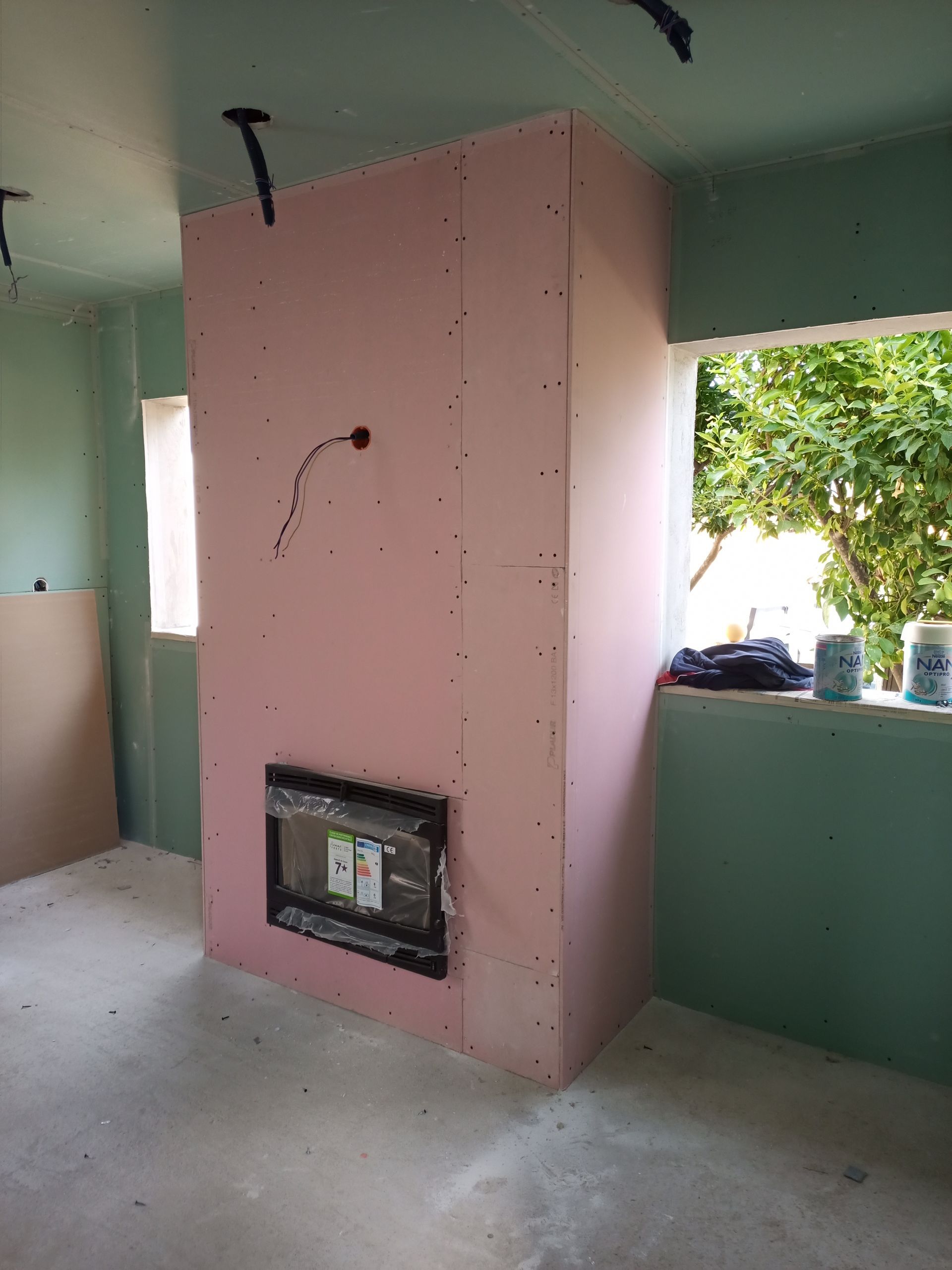 Uma estrutura de gesso cartonado rosa com um painel elétrico embutido em um cômodo em construção, com uma janela.