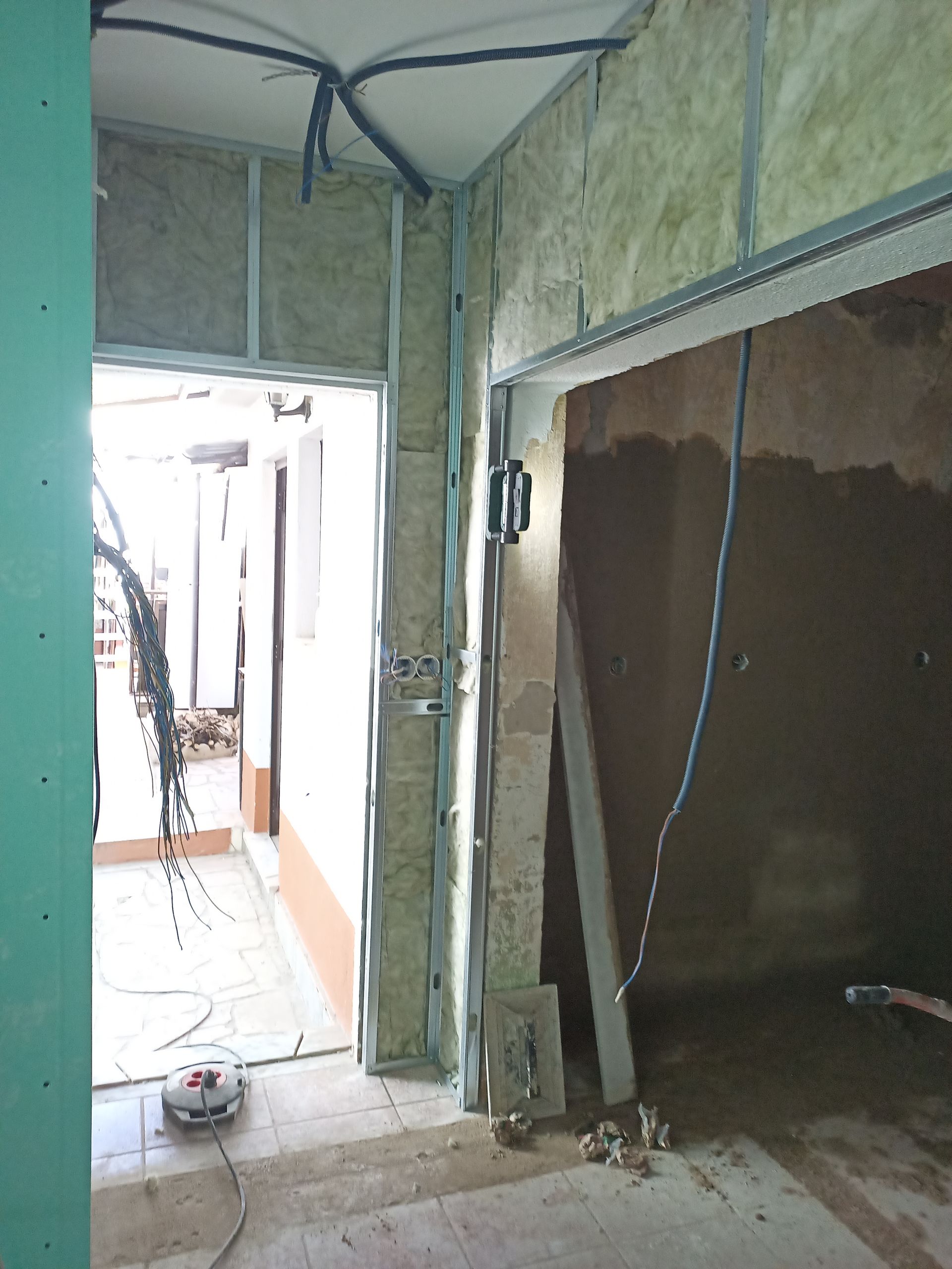 Interior de obra; portas abertas, isolamento, fiação elétrica, paredes inacabadas.