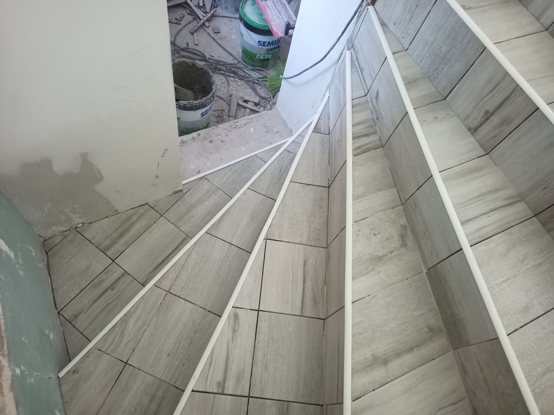 Escada em espiral com degraus revestidos de azulejos e acabamento branco, vista de cima, em construção.