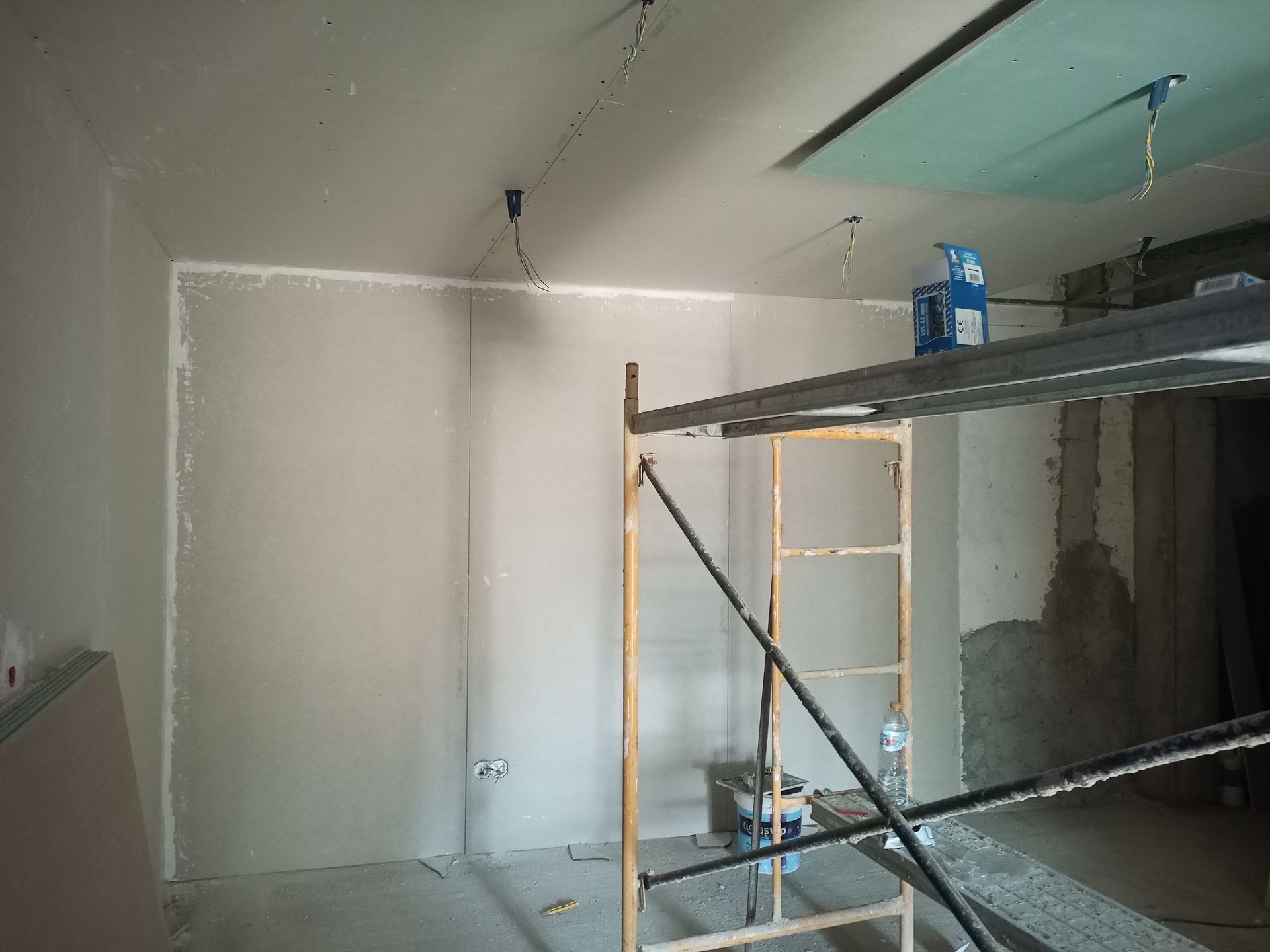 Construção de interiores: Instalação de drywall em um cômodo, com presença de andaimes.