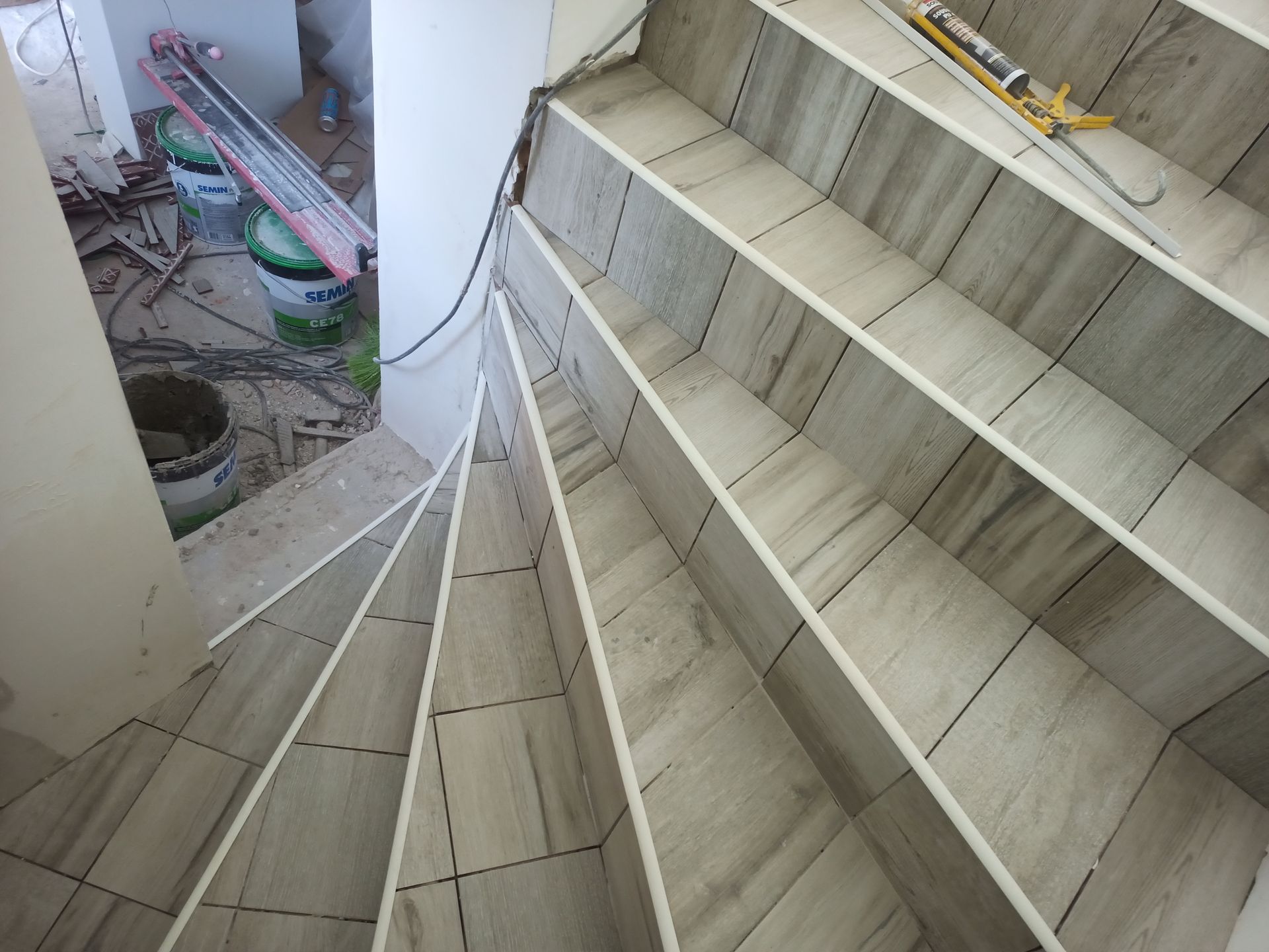 Escada em espiral com degraus revestidos de azulejos e espelhos brancos; materiais de construção visíveis.