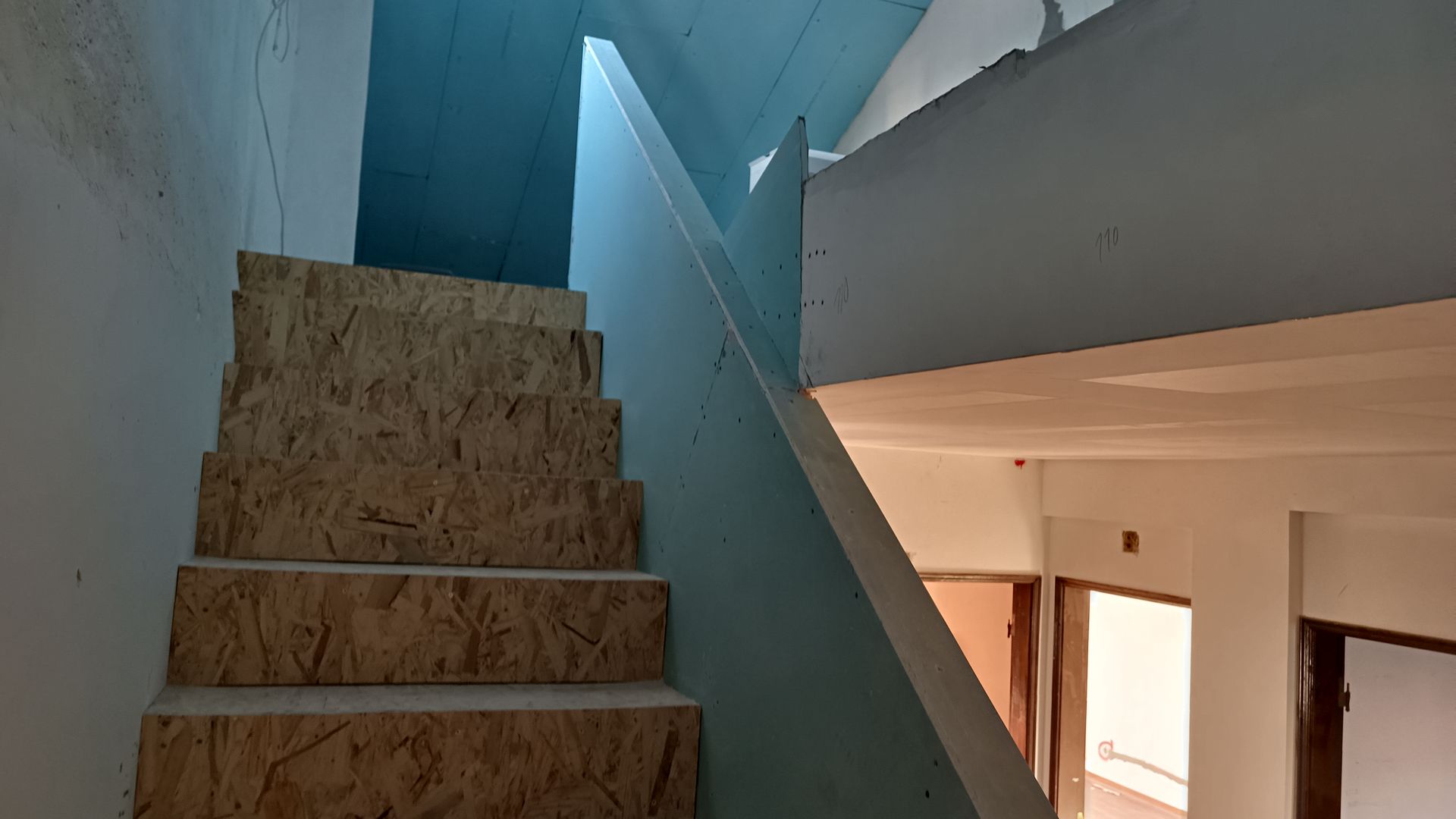 Escada com degraus de aglomerado e teto azul, que leva ao segundo andar.