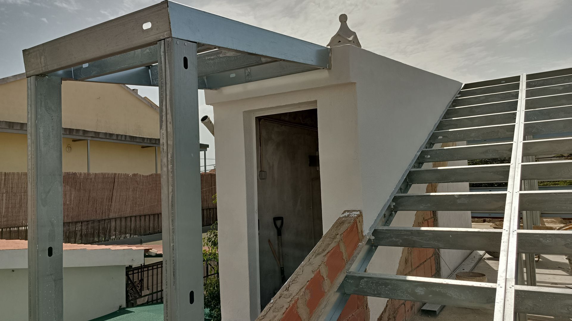 Escada e estrutura metálica que dão acesso a um edifício com porta de entrada, situado num telhado.