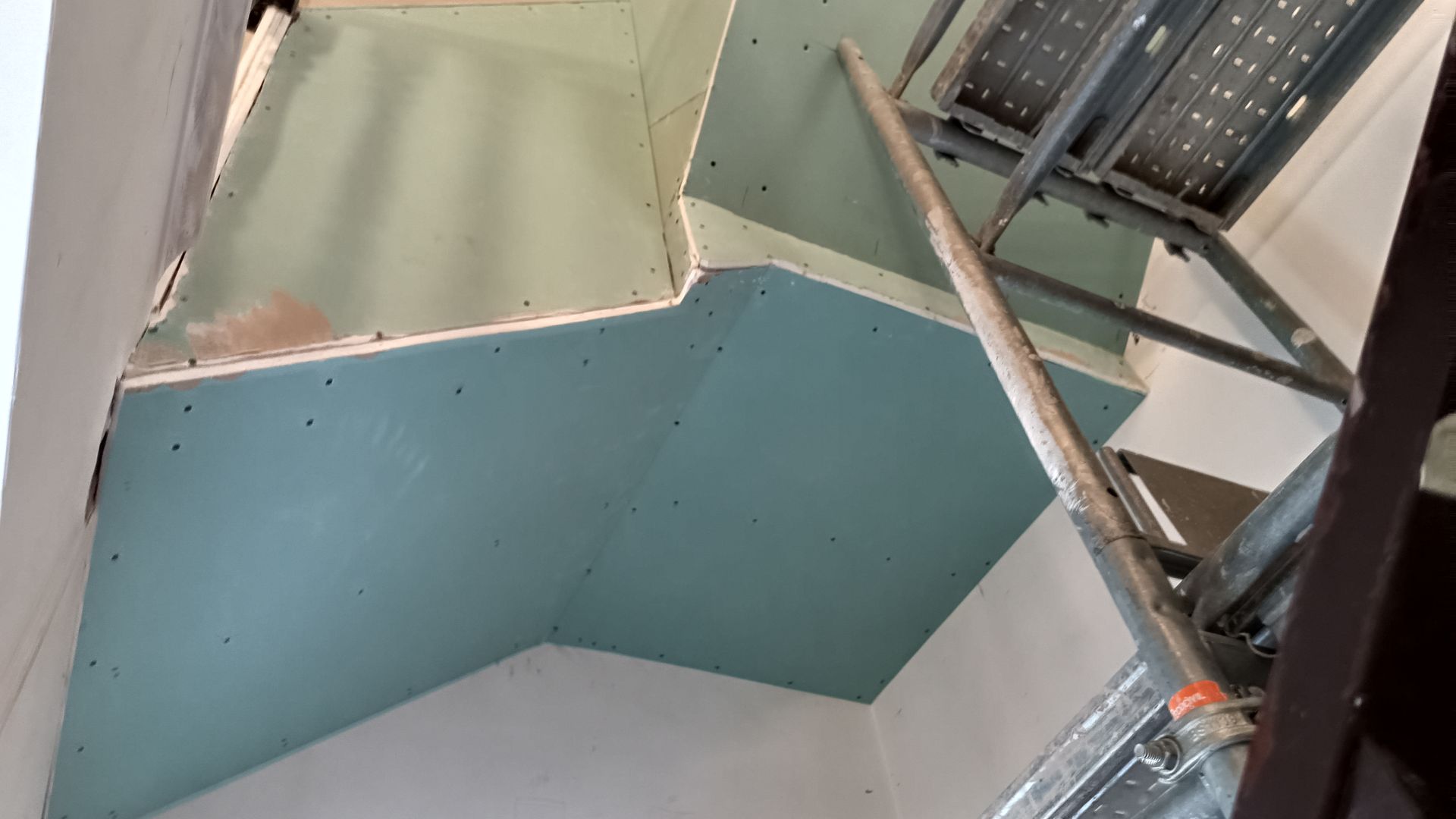 Um teto parcialmente construído com drywall azul e um andaime metálico.