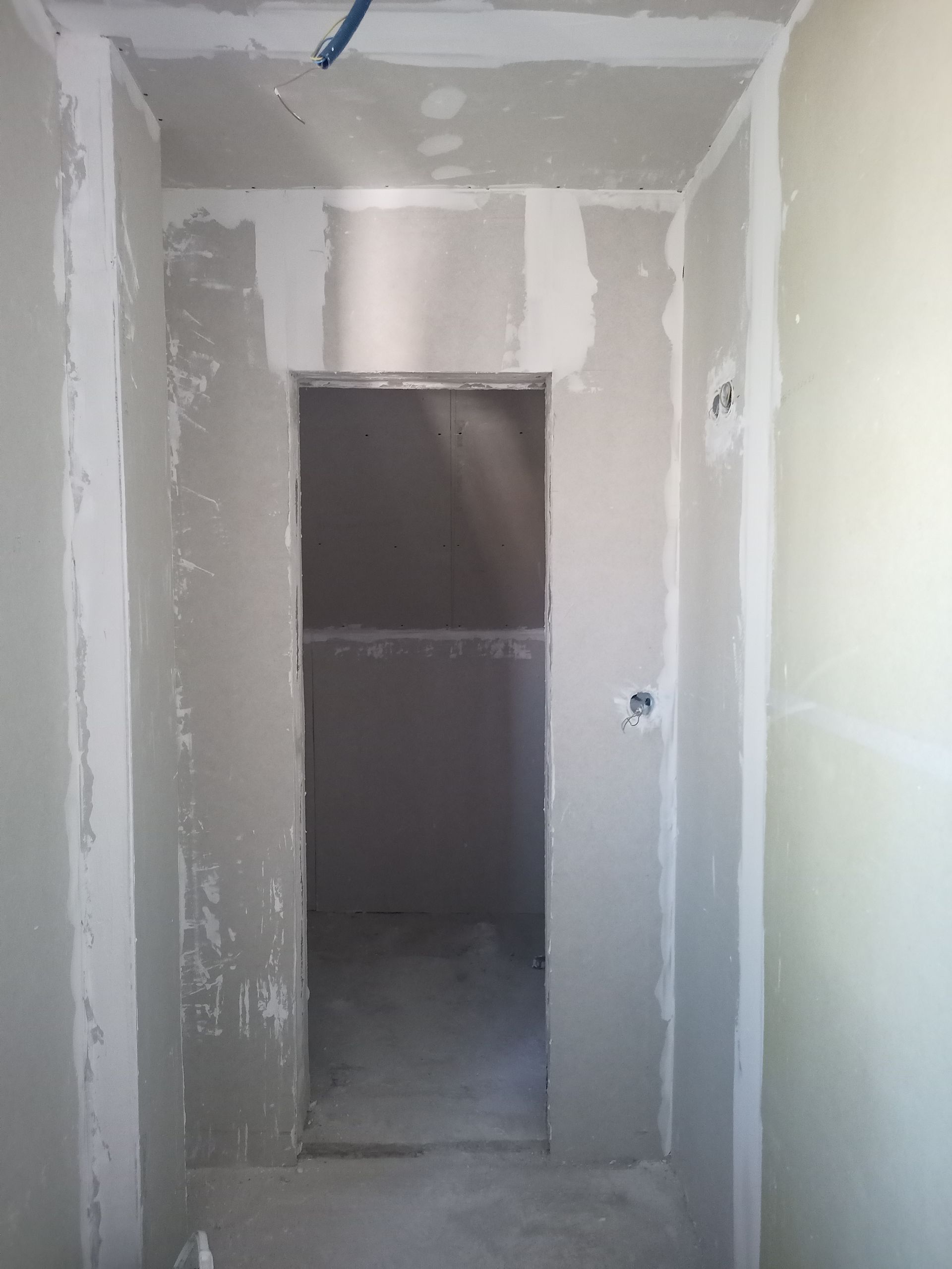 Porta em construção, drywall instalado, com reboco inacabado.