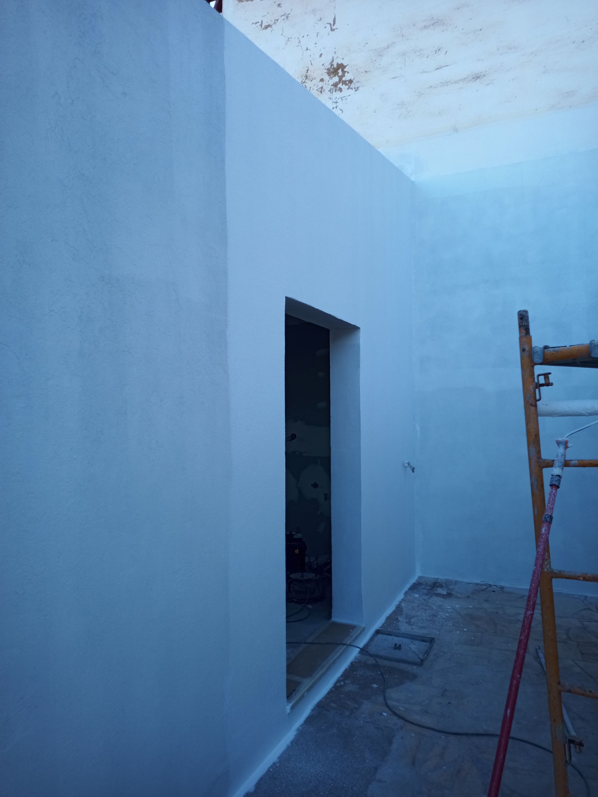 Um quarto pintado de branco com uma porta aberta. Uma escada está encostada na parede.