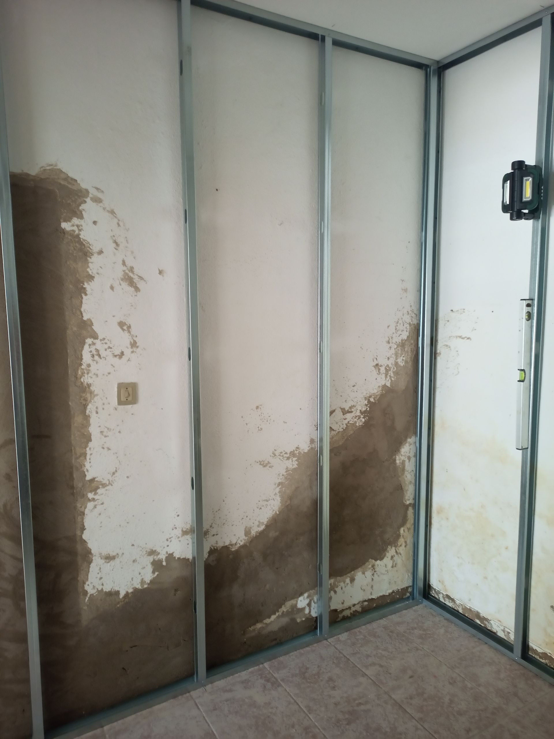 Quarto interior com estrutura de metal e danos causados ​​pela água na parede de gesso.