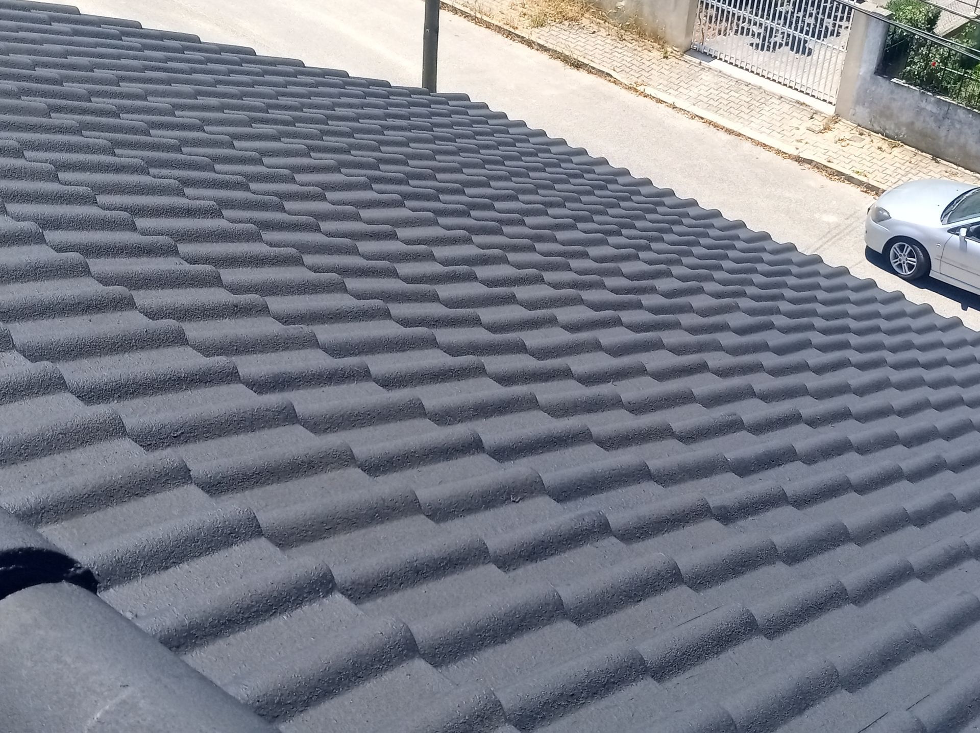 Telhado de telhas cinzentas em um prédio, com um carro estacionado nas proximidades, na rua.