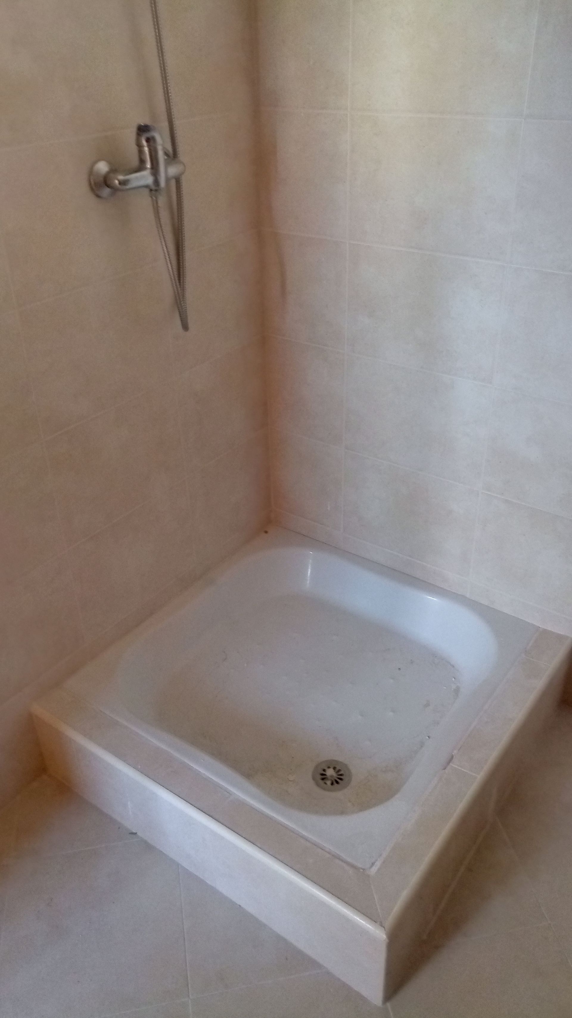 Cabine de duche com soleira baixa, chuveiro de mão e paredes e chão de cor clara.