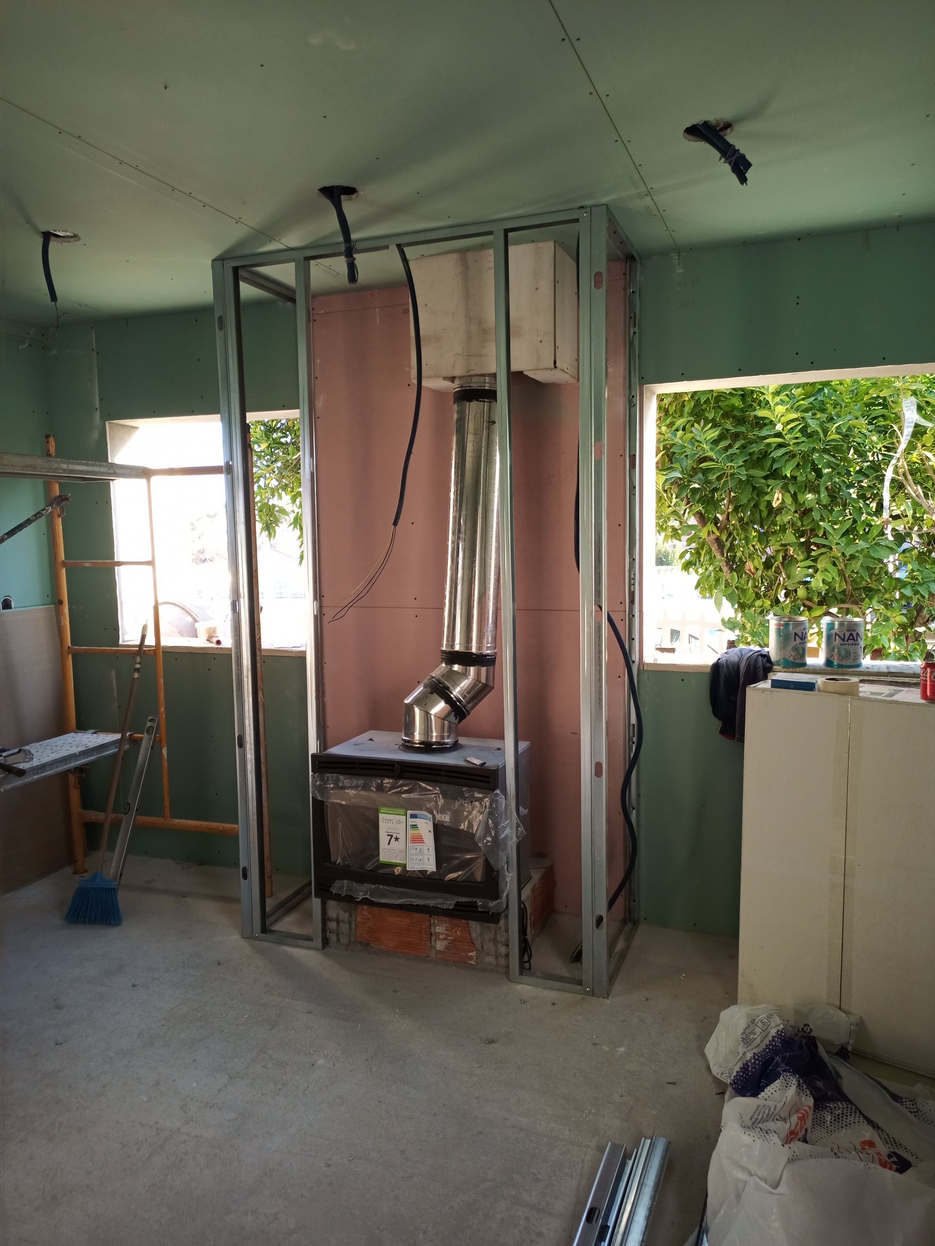 Construção de uma lareira com estrutura metálica, chaminé e base de tijolos em um cômodo. A fiação elétrica está visível.