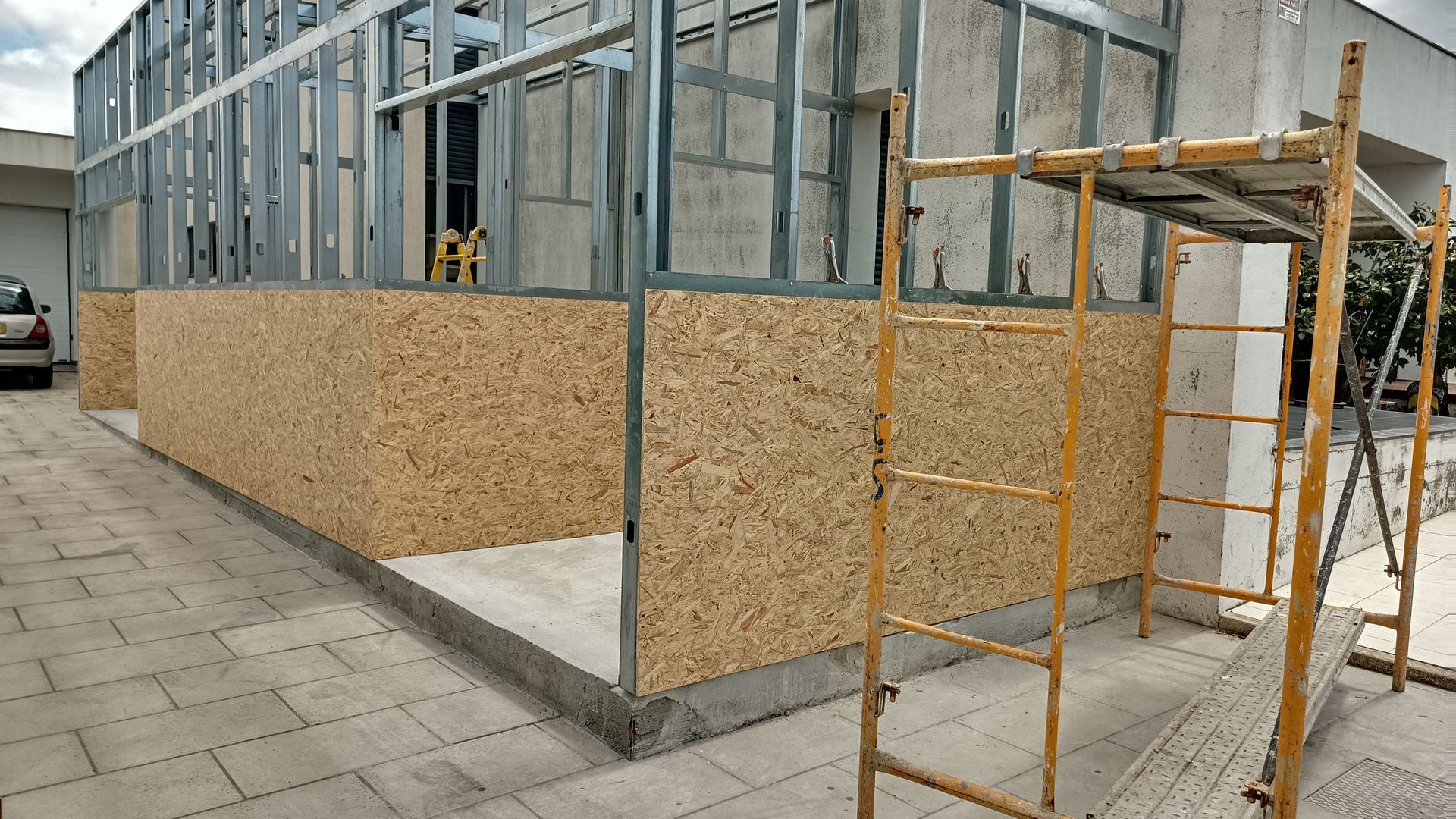 Canteiro de obras com estrutura metálica, painéis de madeira e andaimes.