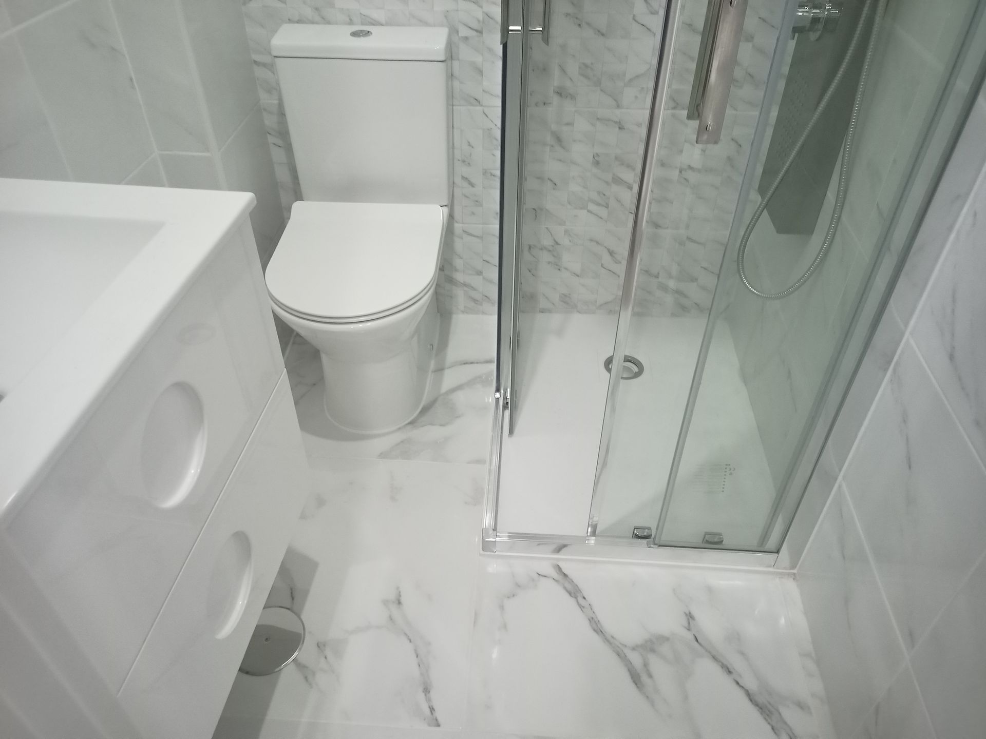 Banheiro branco com vaso sanitário, pia e box de vidro.