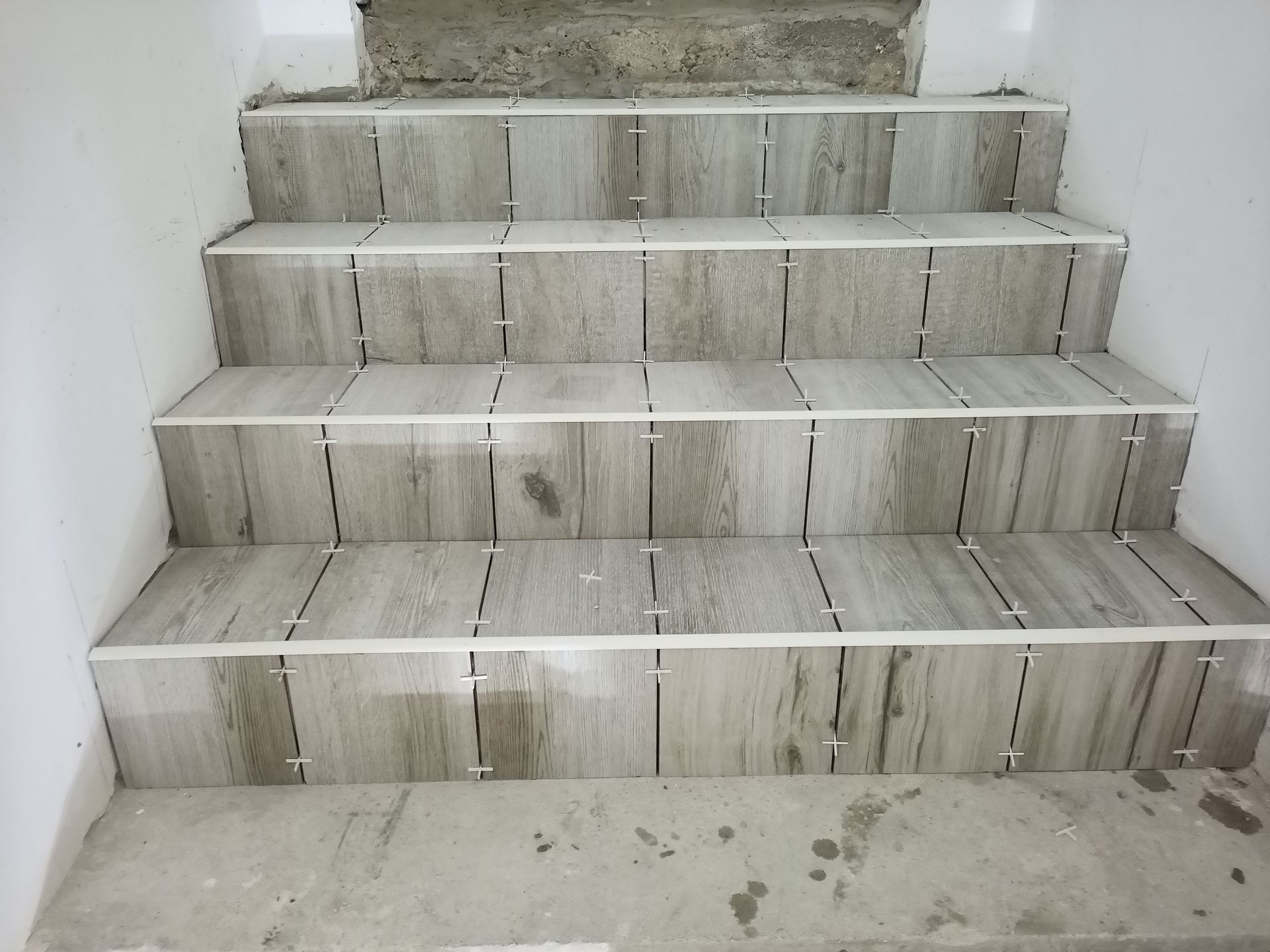 Escada com ladrilhos retangulares cinza-claro, espaçadores brancos, concreto e paredes brancas.