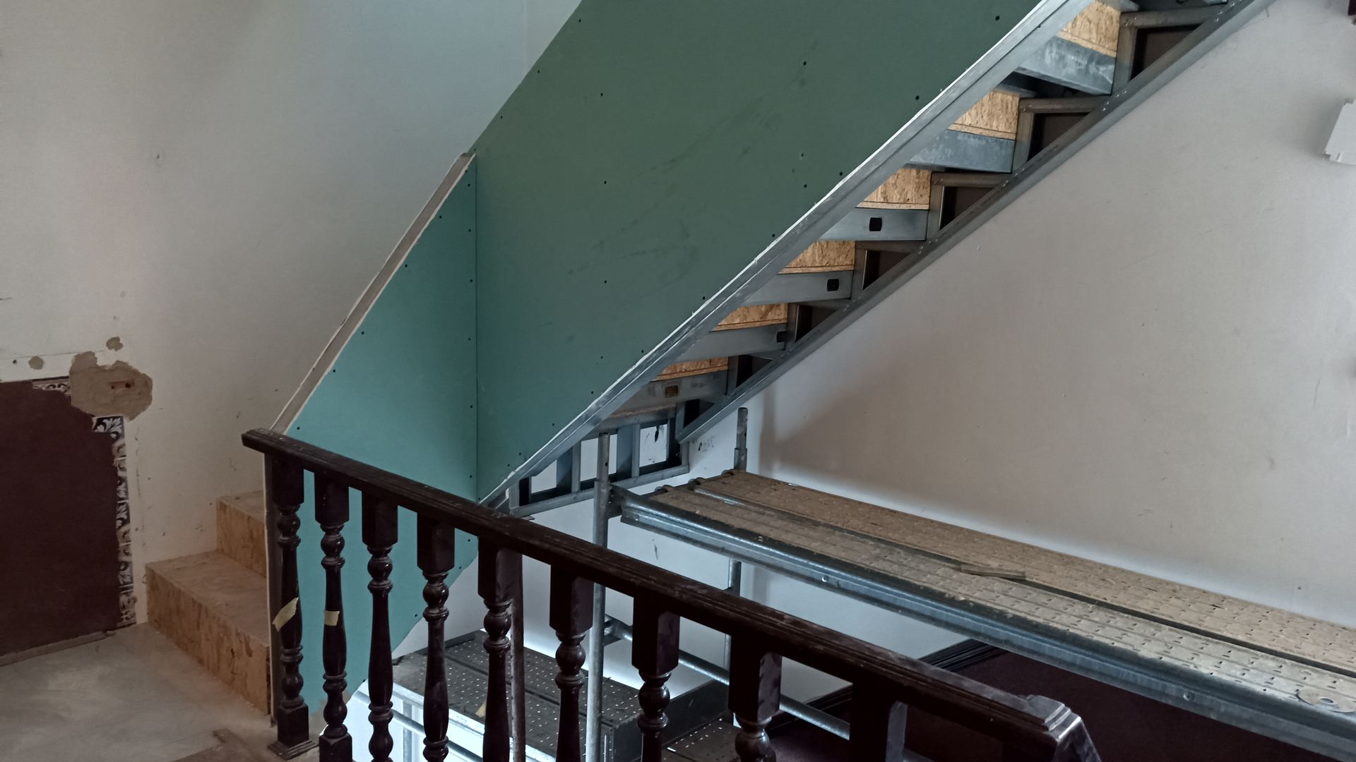 Construção de escada em um edifício. Estrutura metálica com drywall, corrimão de madeira e degraus.