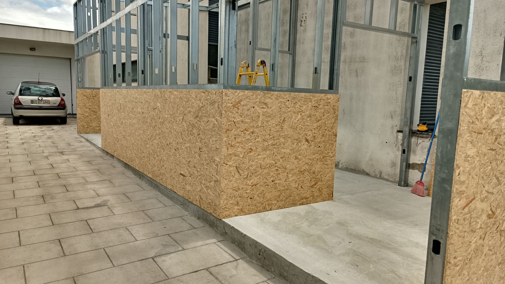 Construção exterior: estrutura metálica e painéis de madeira; veículo ao fundo.