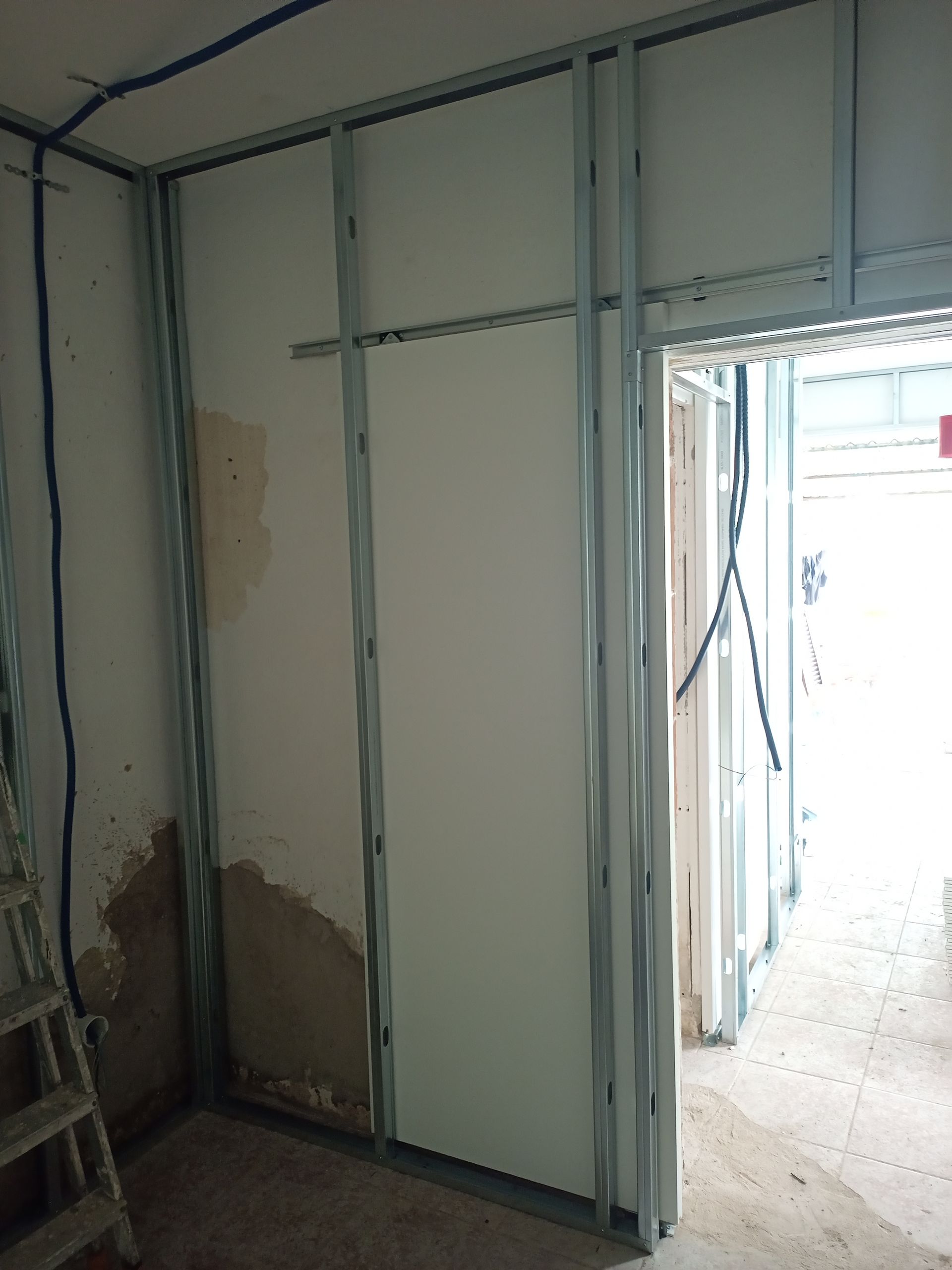 Vista interna de um cômodo em construção com estrutura metálica e drywall. Uma porta é visível.