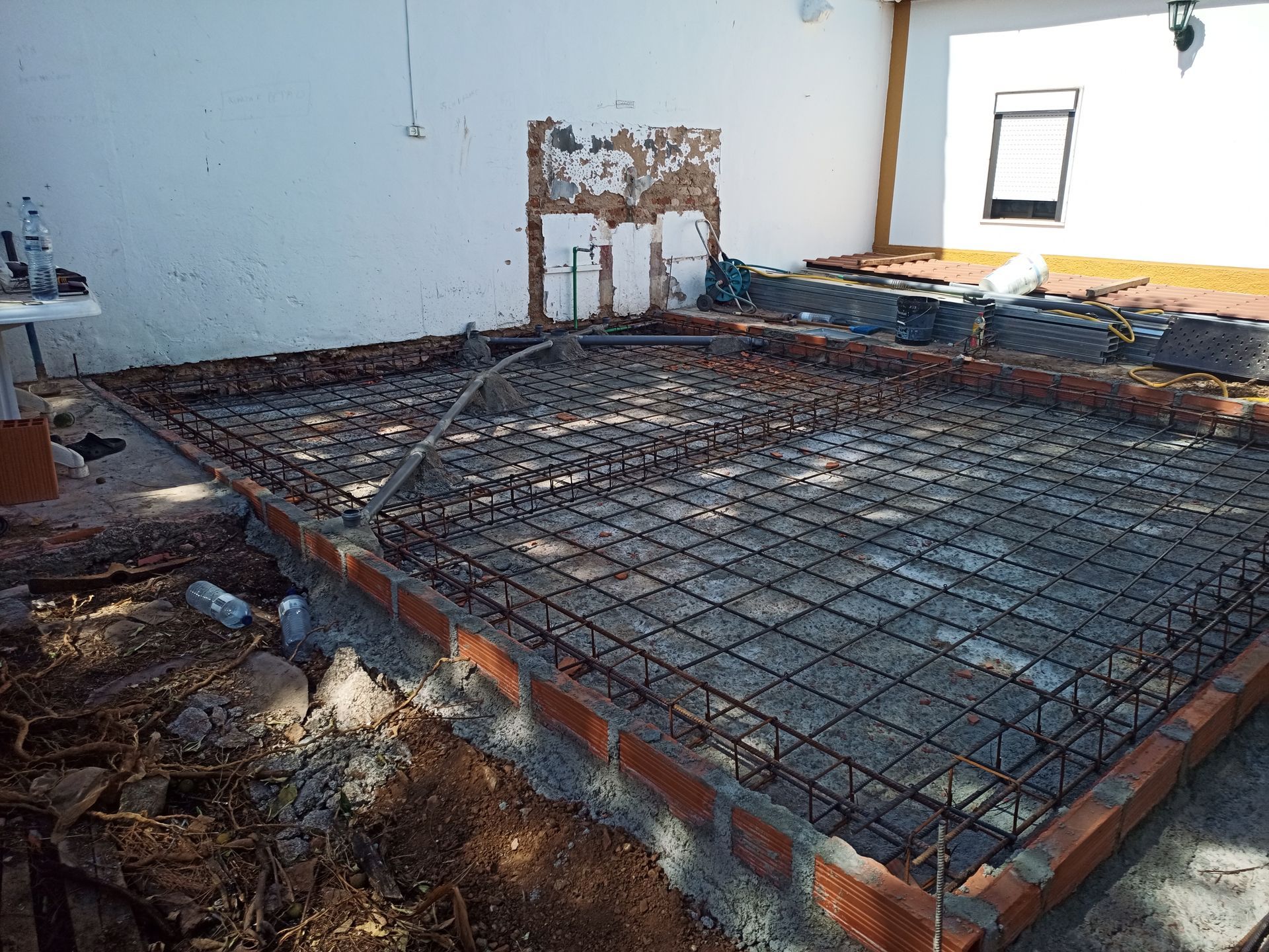 Canteiro de obras: bordas de tijolos delimitam a estrutura de vergalhões de aço, pronta para receber o piso de concreto, em área externa.