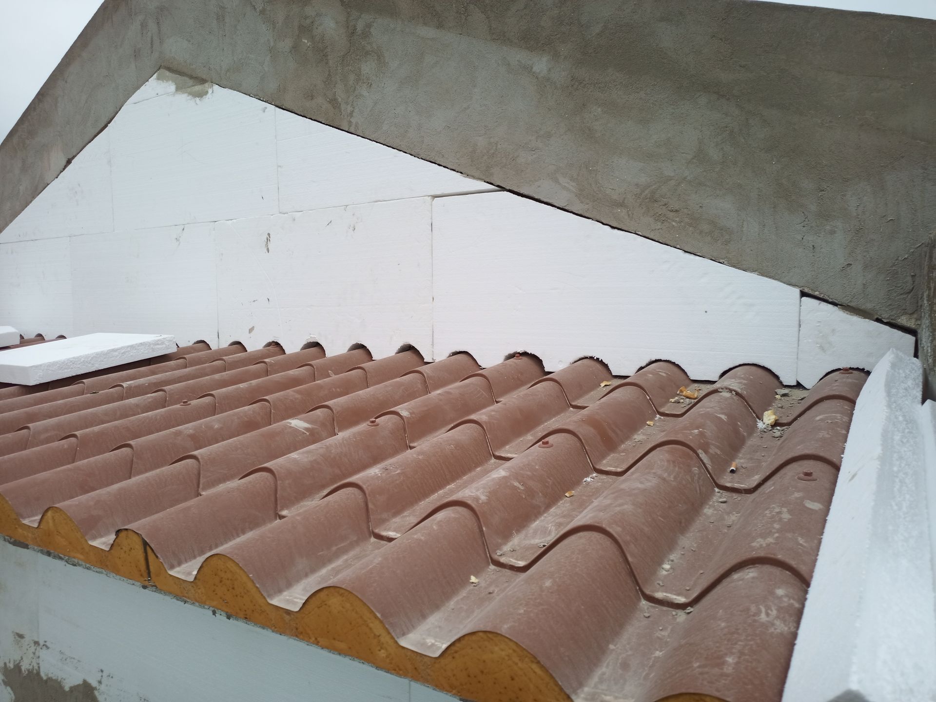 Telhado de telhas marrons com isolamento de espuma branca e viga de concreto.