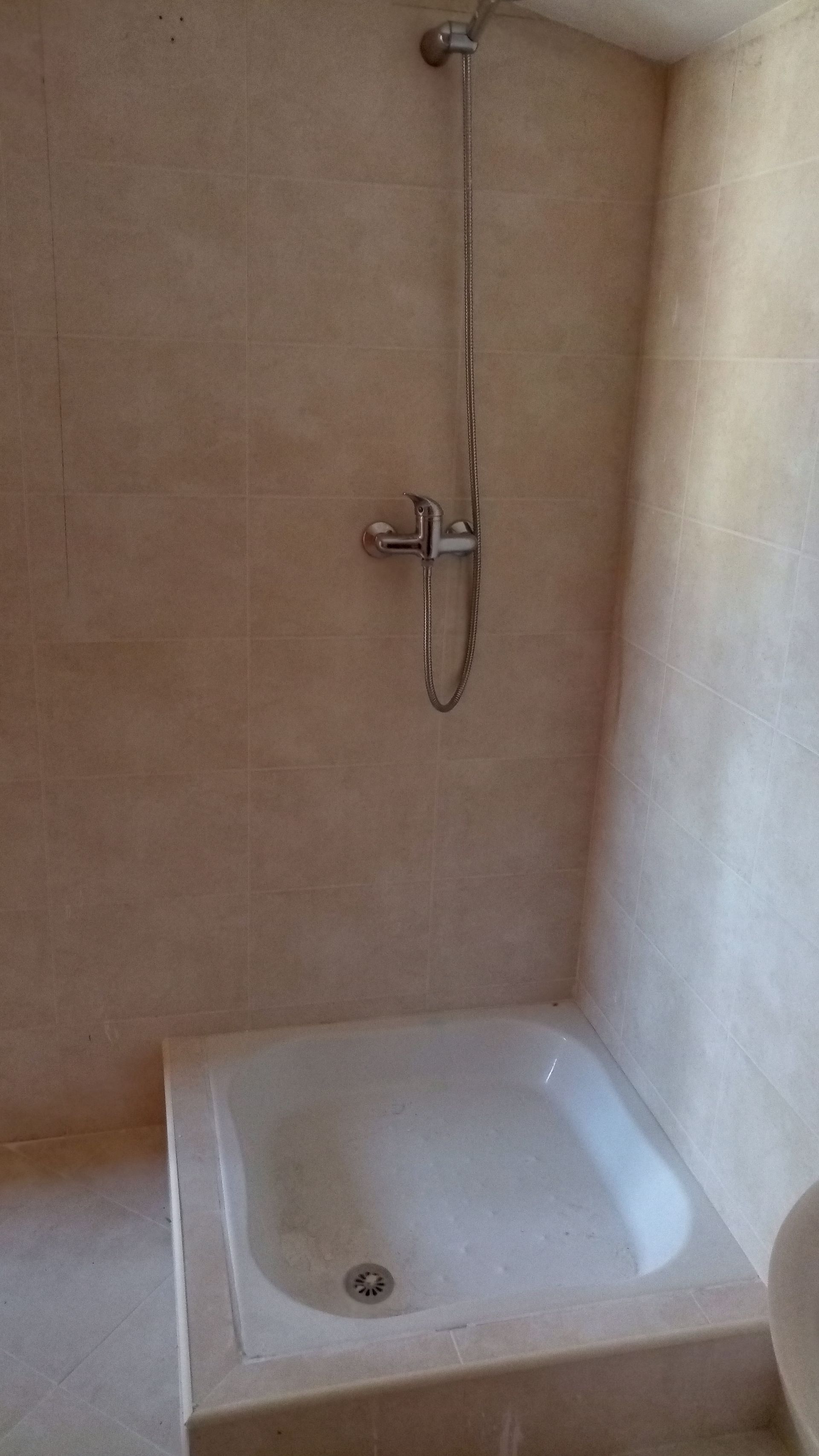 Cabine de duche com paredes revestidas a azulejos bege, lavatório branco e acessórios de duche prateados.